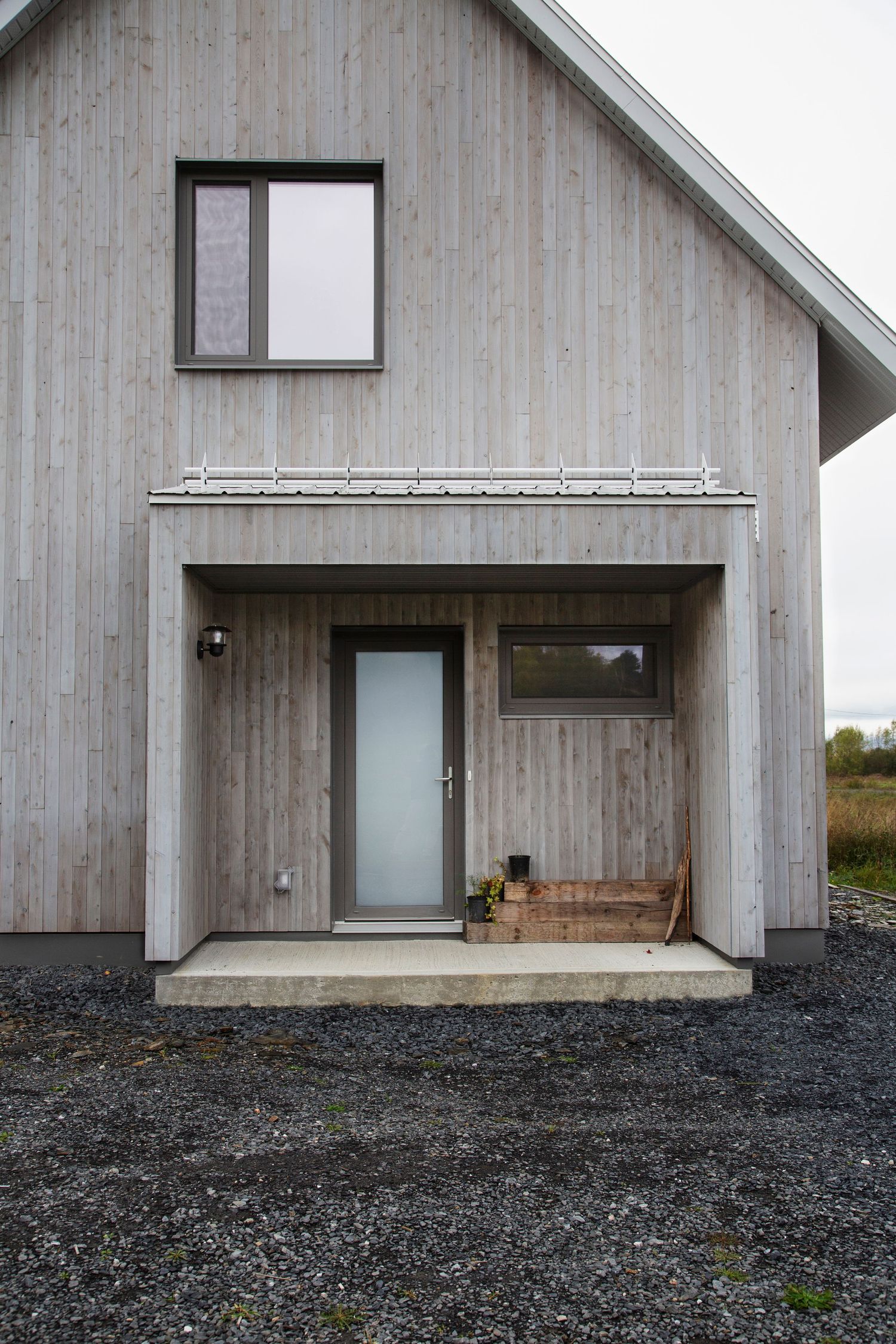 Contemporary barn-style house with weathered wood siding and a covered entrance porch.