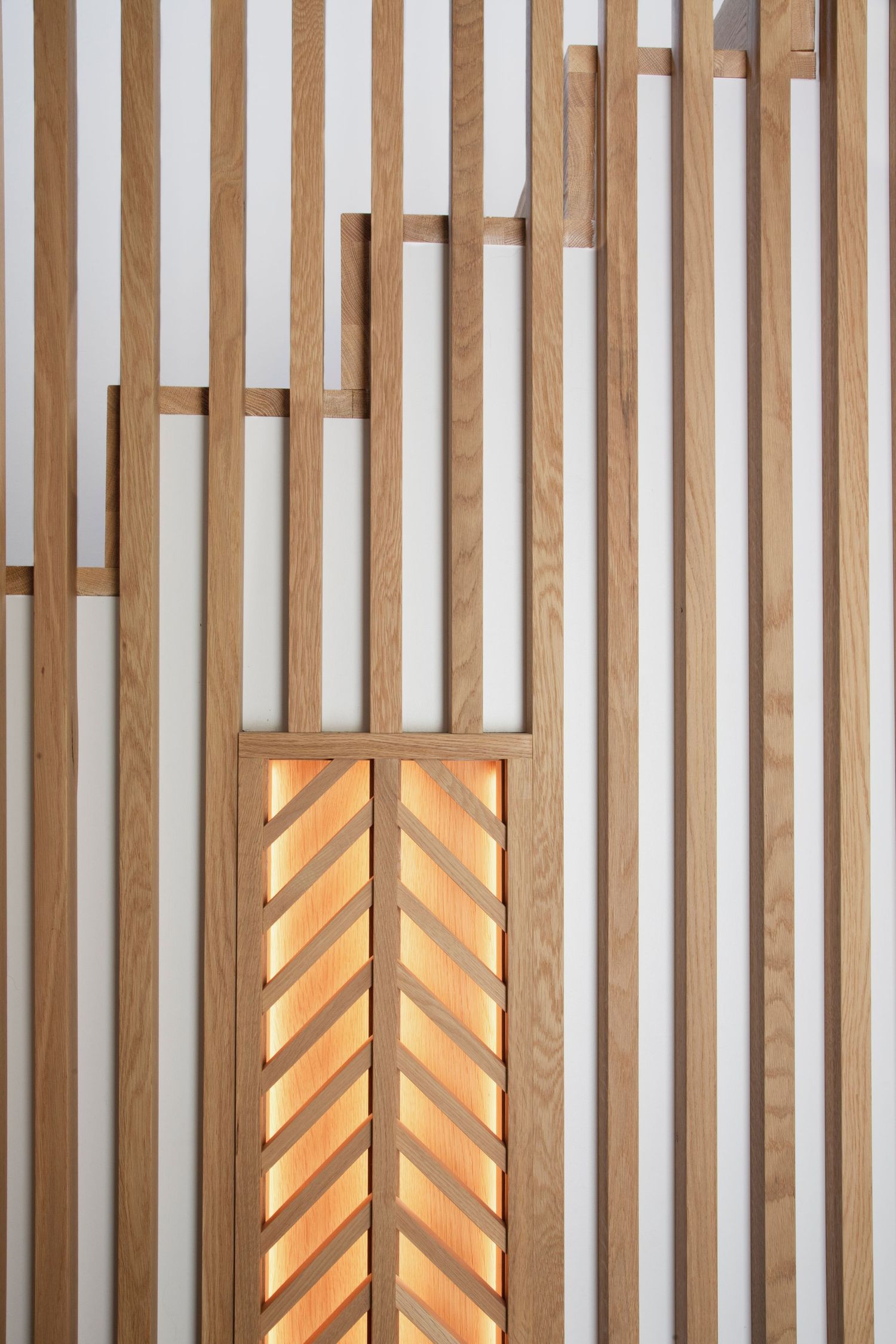 Modern wooden slat wall with illuminated chevron pattern accent lighting.