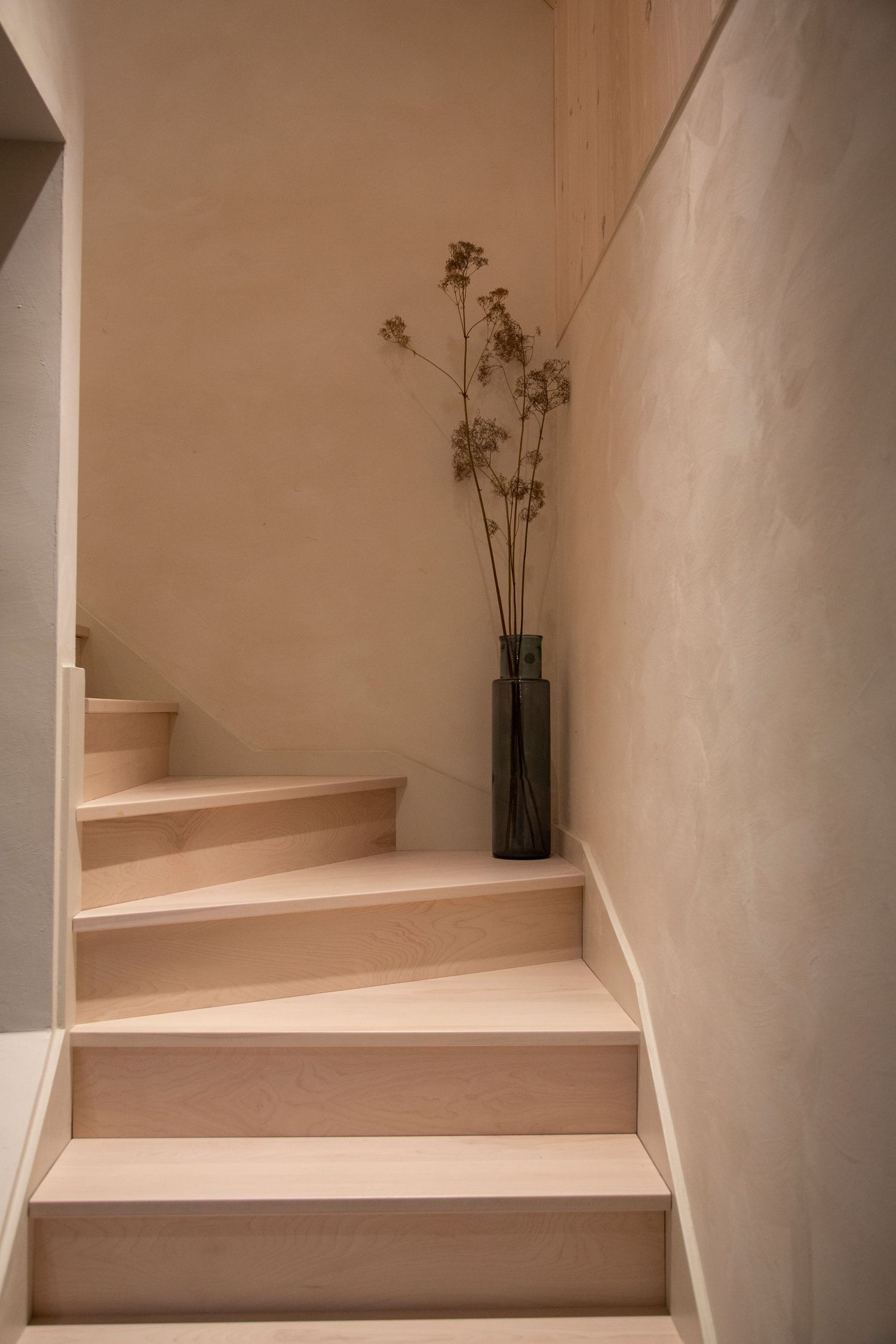 Modern wooden staircase with light wood steps and white walls in a minimalist interior.