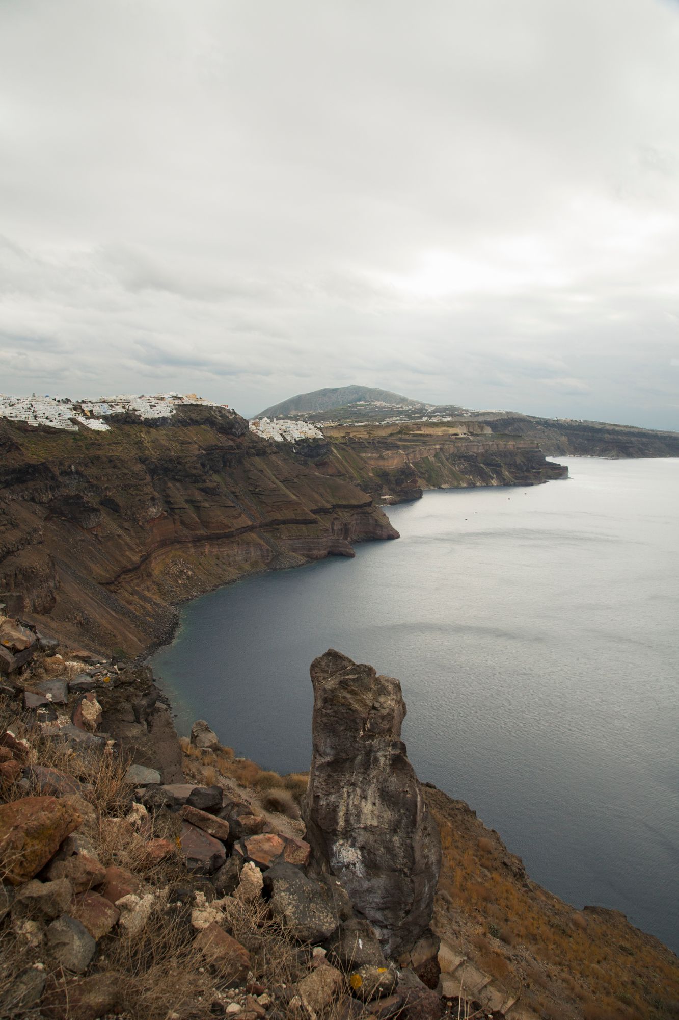 Dark volcanic cliffs overlook a dramatic coastline with white buildings visible in the distance.