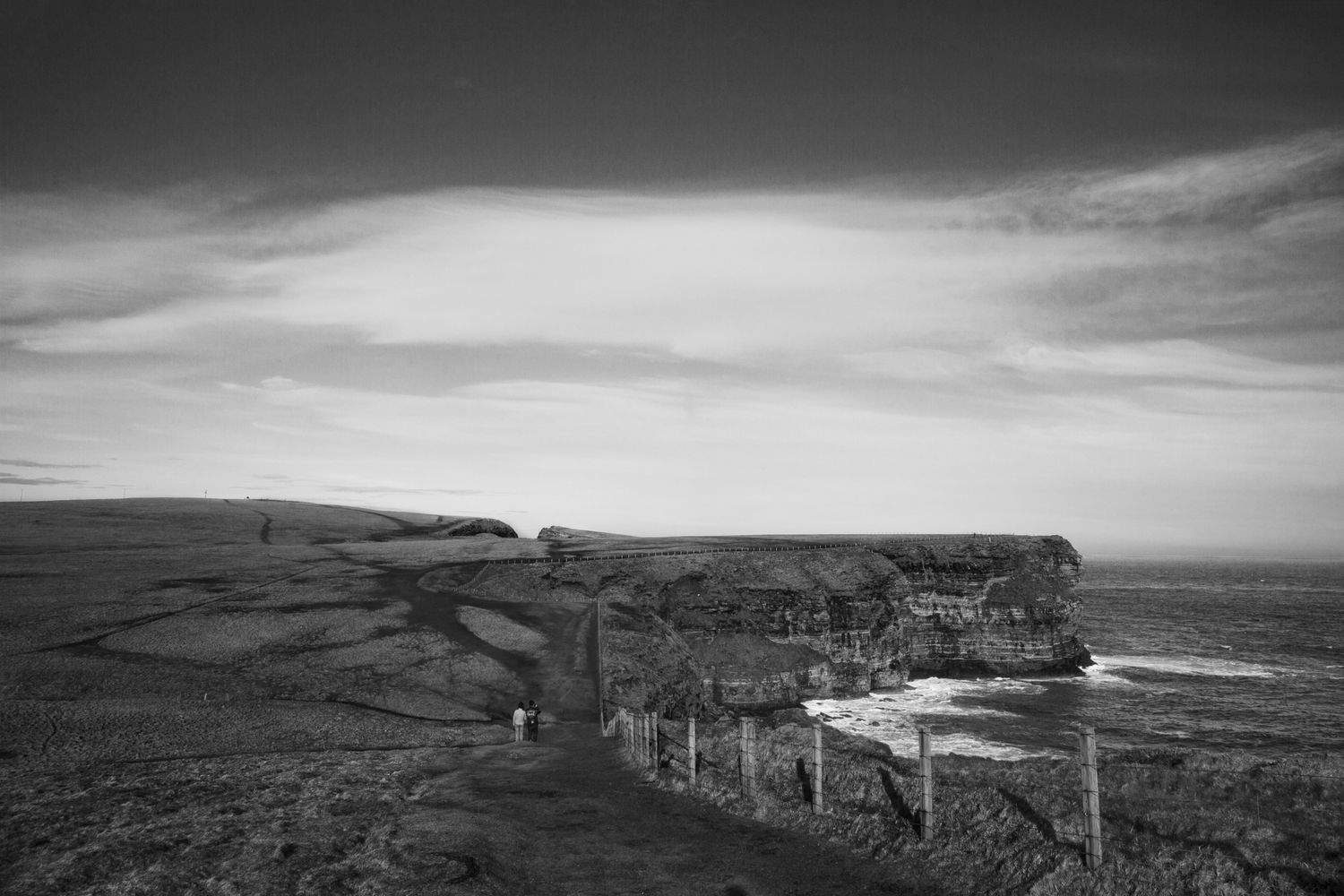 A dramatic black and white coastal landscape with rugged cliffs and a winding path along the Irish coastline.