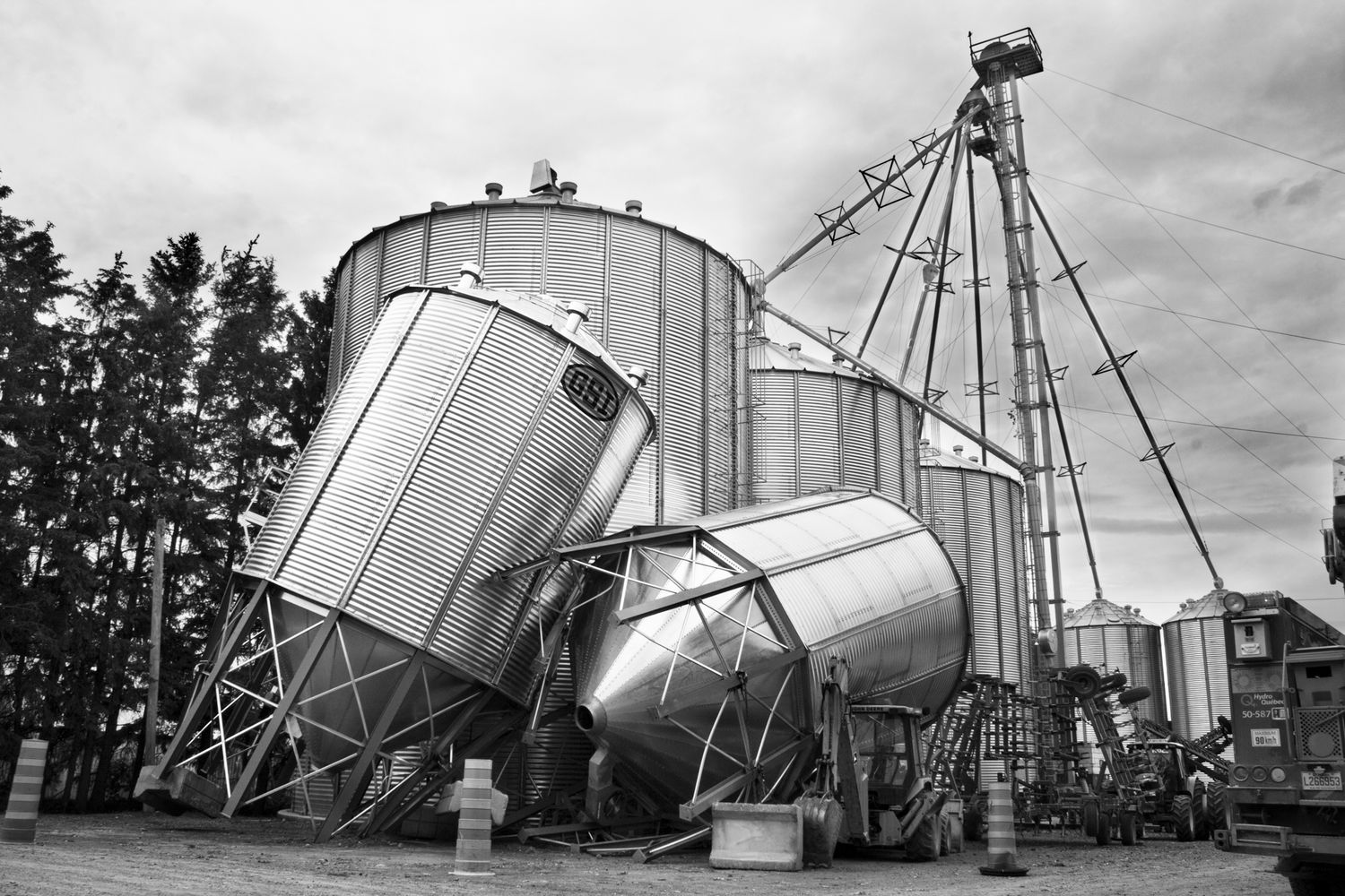 A dramatic black and white photo series showing grain silos and farm equipment at different angles against a cloudy sky.