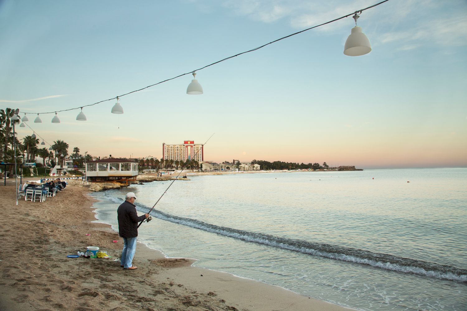 Beach promenade with string lights at sunset overlooking calm ocean waters.