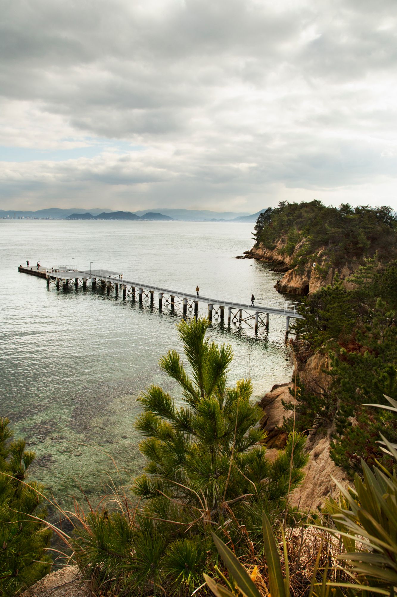 Coastal landscape with wooden pier extending into blue ocean waters and rocky cliffs.