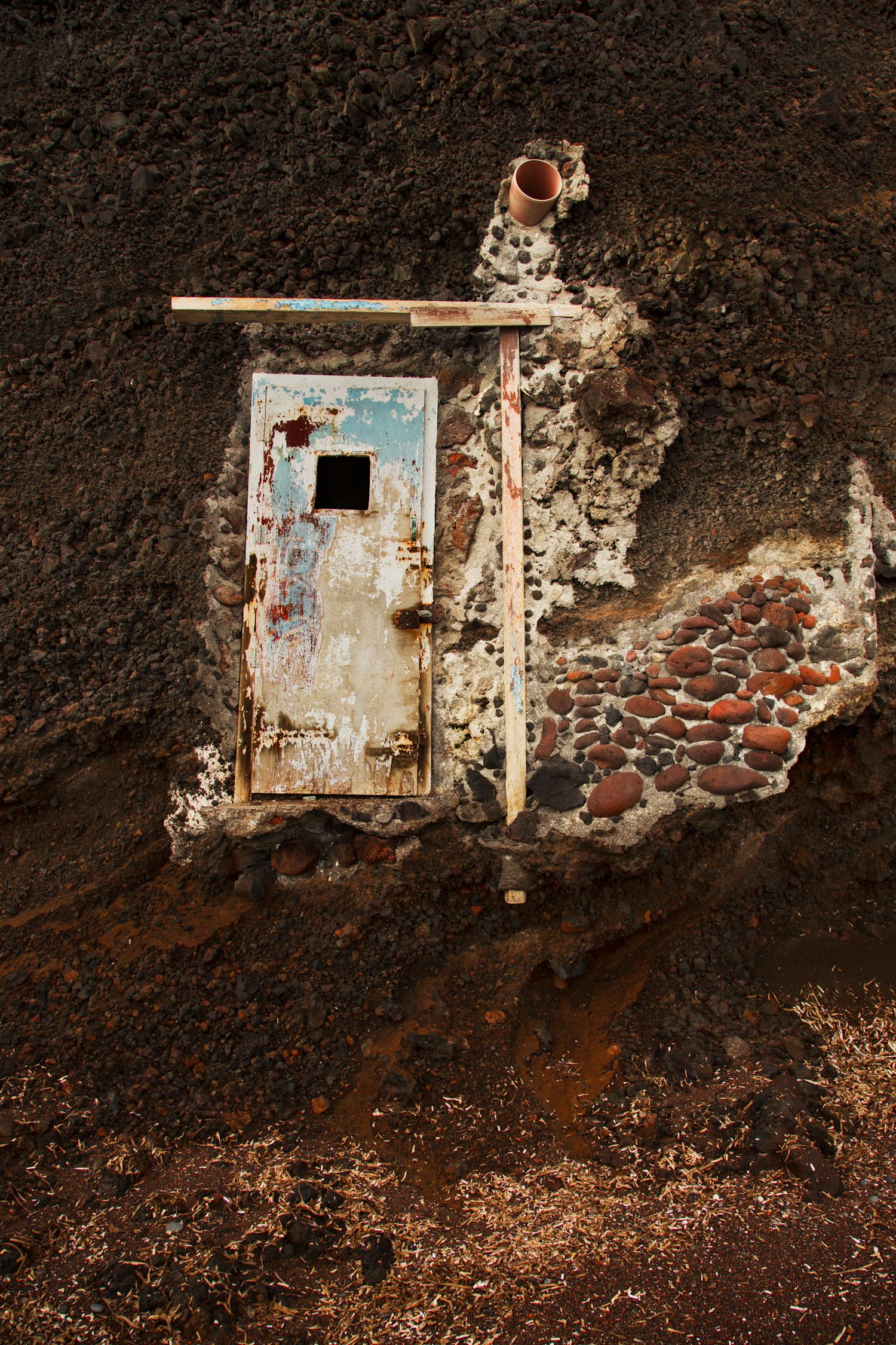 Abandoned stone bunkers built into red volcanic rocks along a coastal area.
