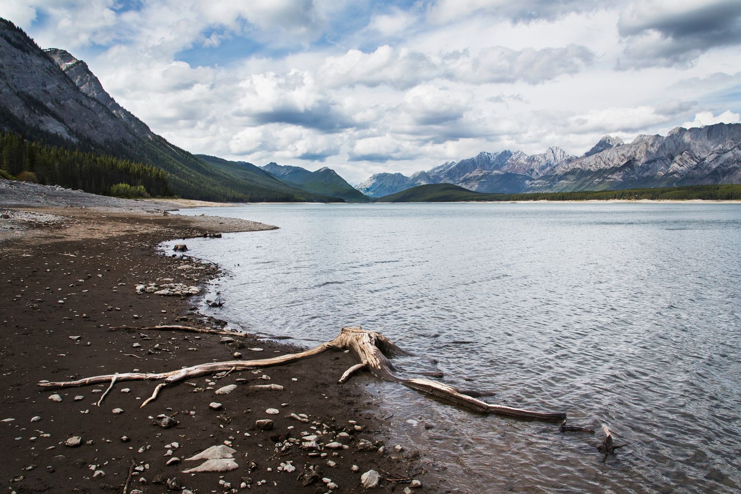 Dramatic mountain landscape reflected in calm lake waters under cloudy skies.
