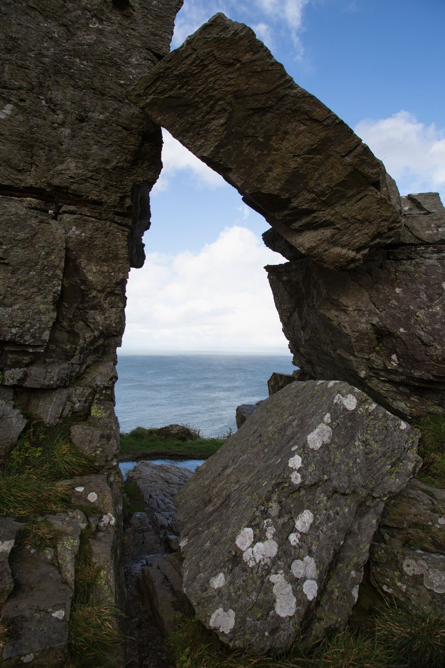Natural rock arch formation on a coastal cliff overlooking the ocean under blue skies.
