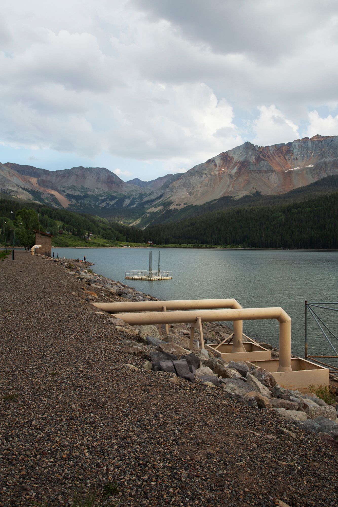 A panoramic sequence of a mountain lake shoreline with metal pipes running along a rocky embankment.