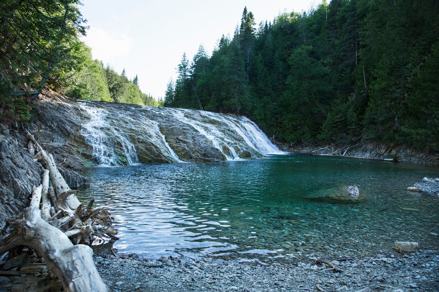 Wide cascading waterfall flows into a turquoise pool surrounded by forest.