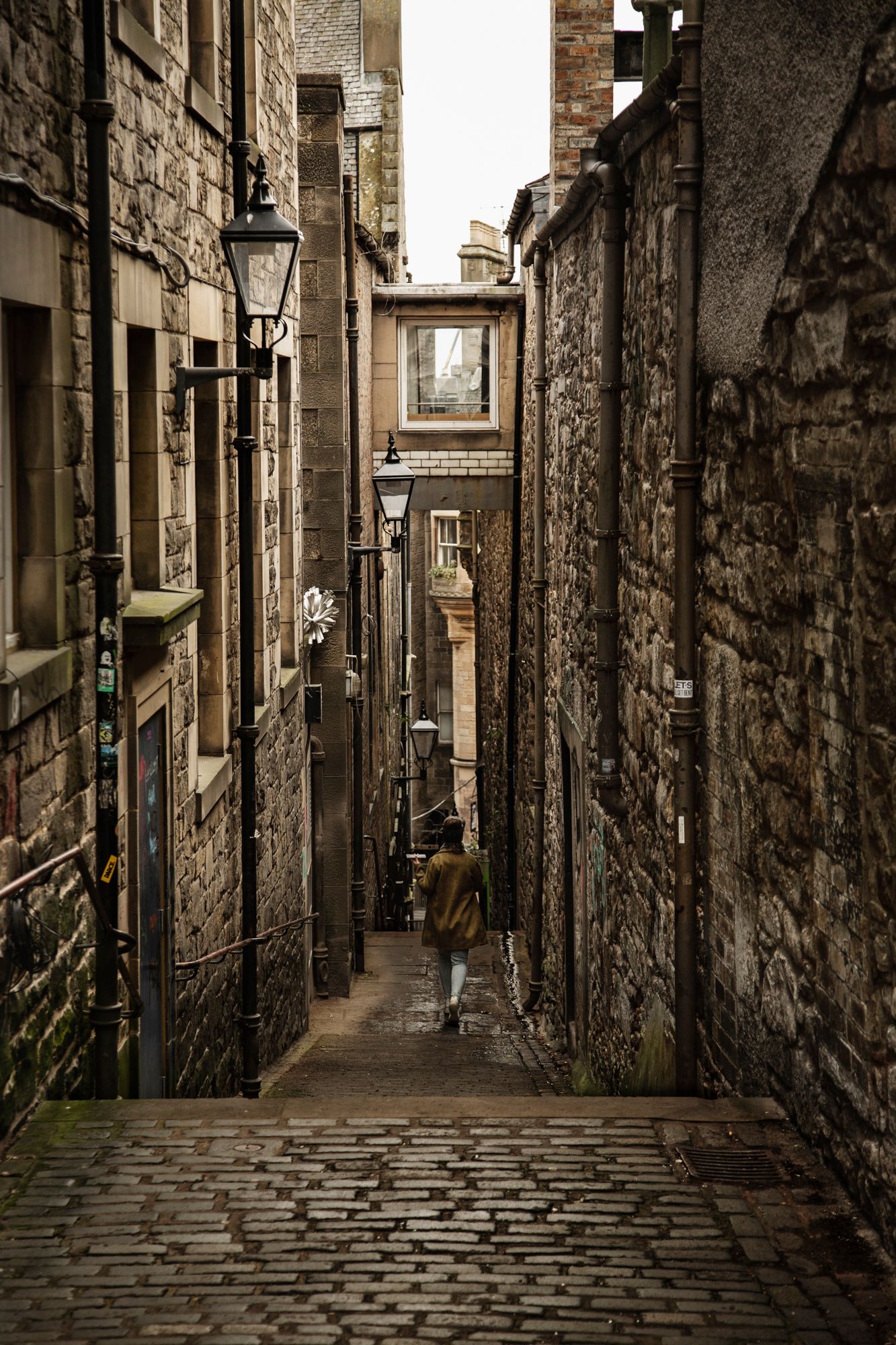 Historic cobblestone alley with stone walls and archways in Edinburgh's medieval Old Town creates moody atmosphere.