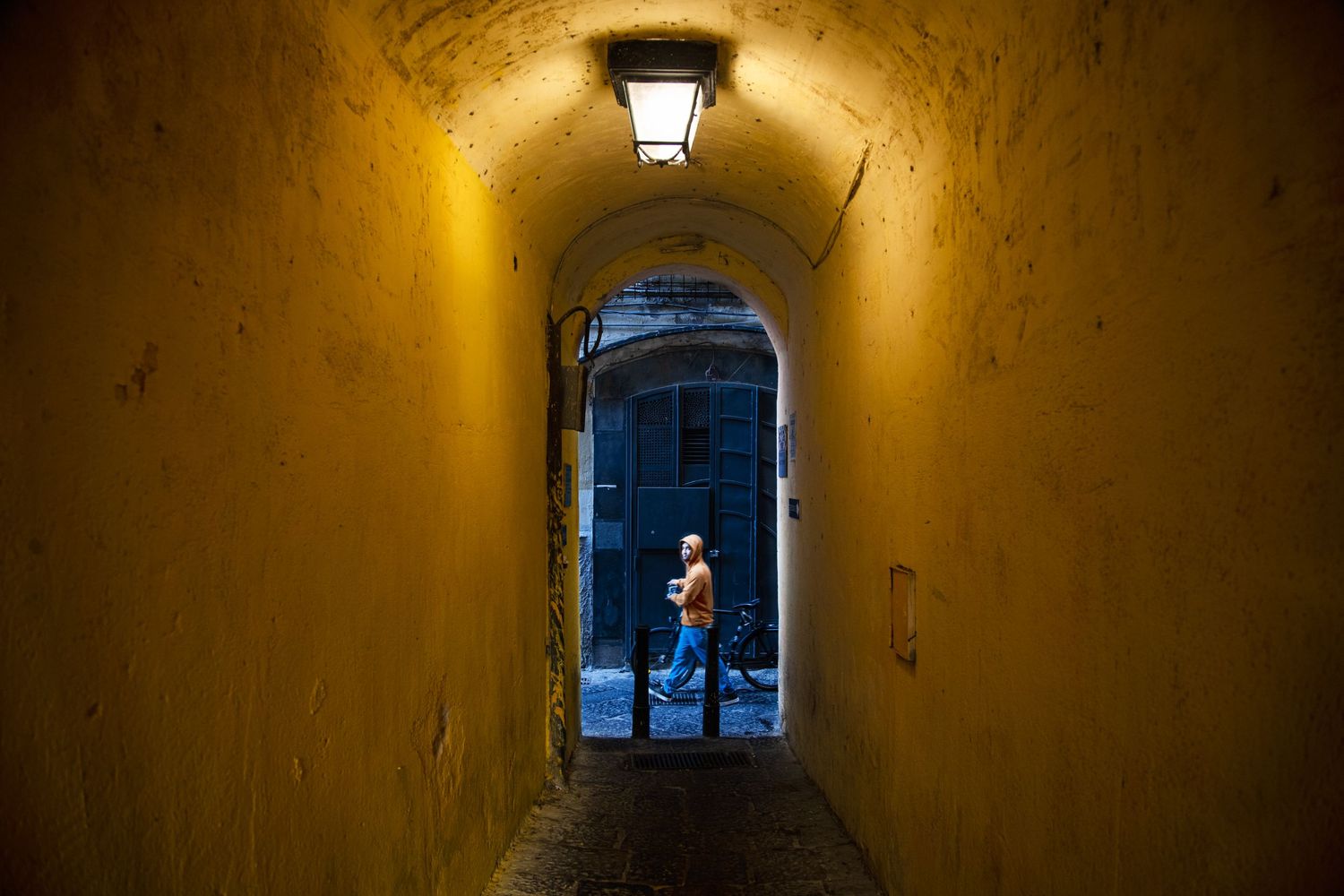 Person silhouetted at end of narrow yellow-lit tunnel archway at night.