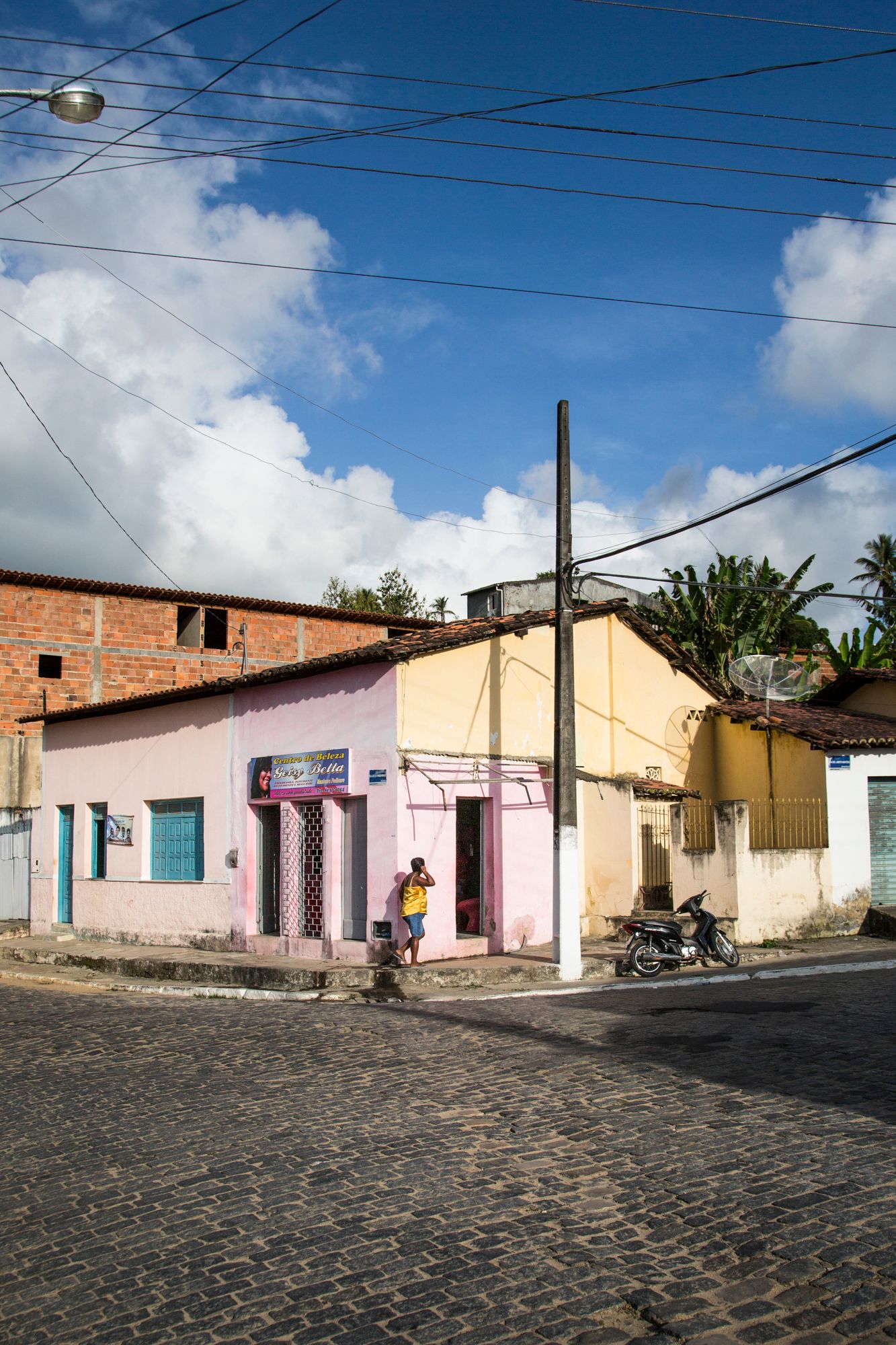 Cobblestone street lined with pastel-colored houses and utility poles in a quiet neighborhood.