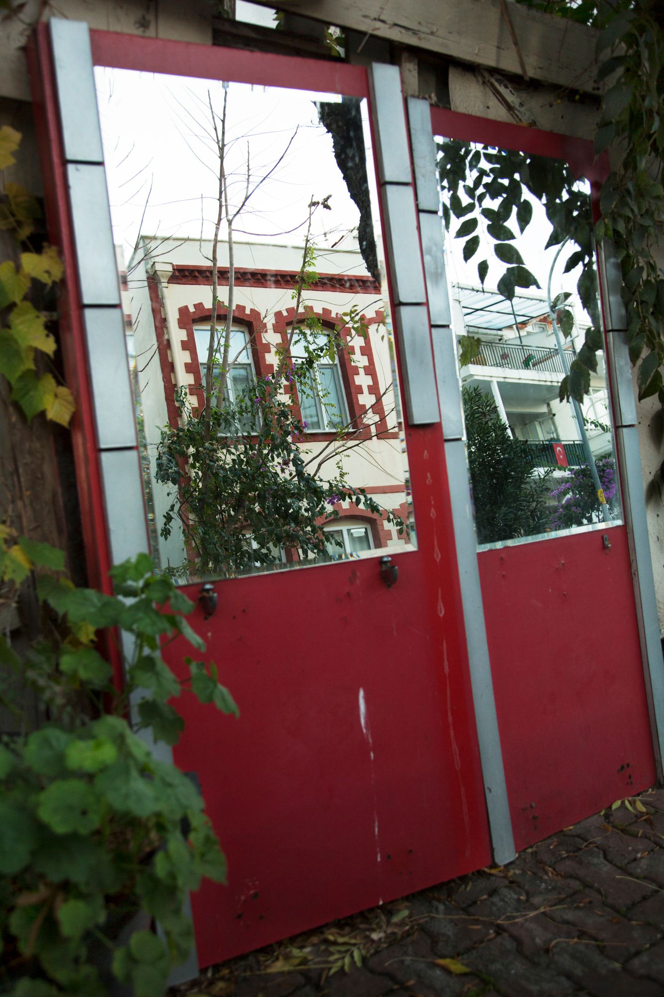 Red panels with windows line an exterior wall covered in climbing vines.