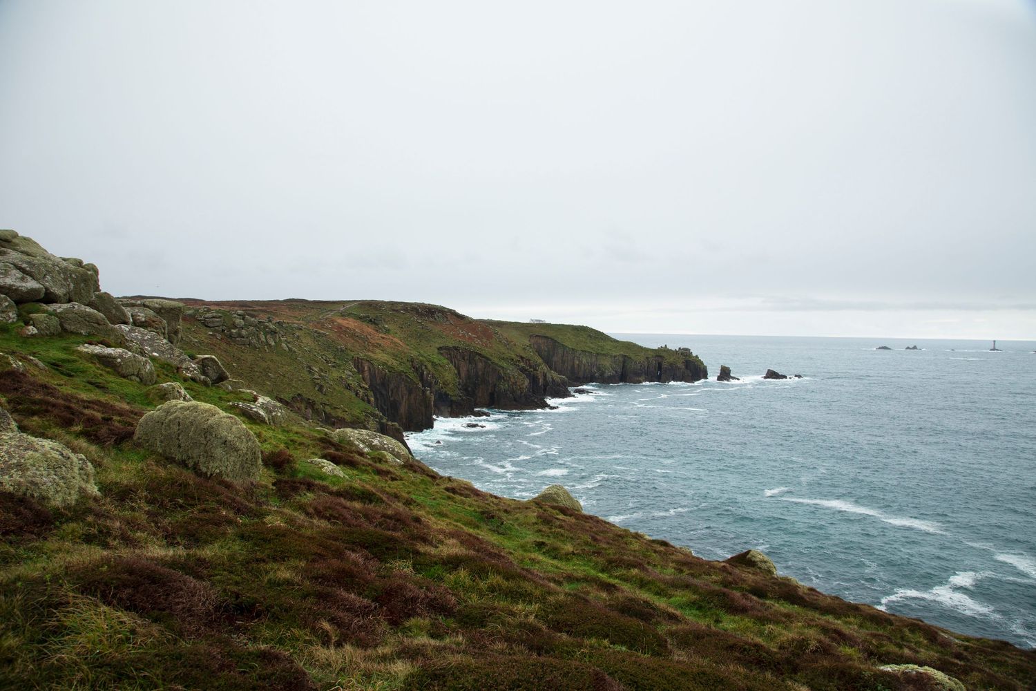 Rugged coastal landscape with waves crashing against rocky cliffs under cloudy skies.