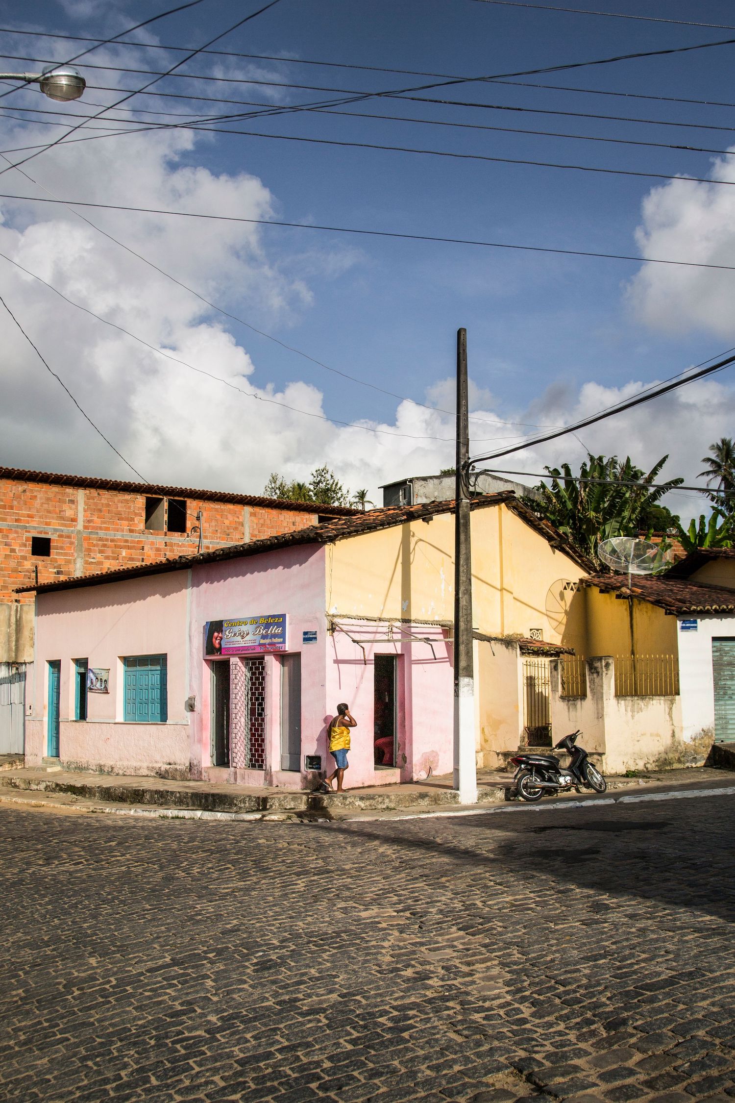 Colorful houses line cobblestone street with power lines overhead in small town.