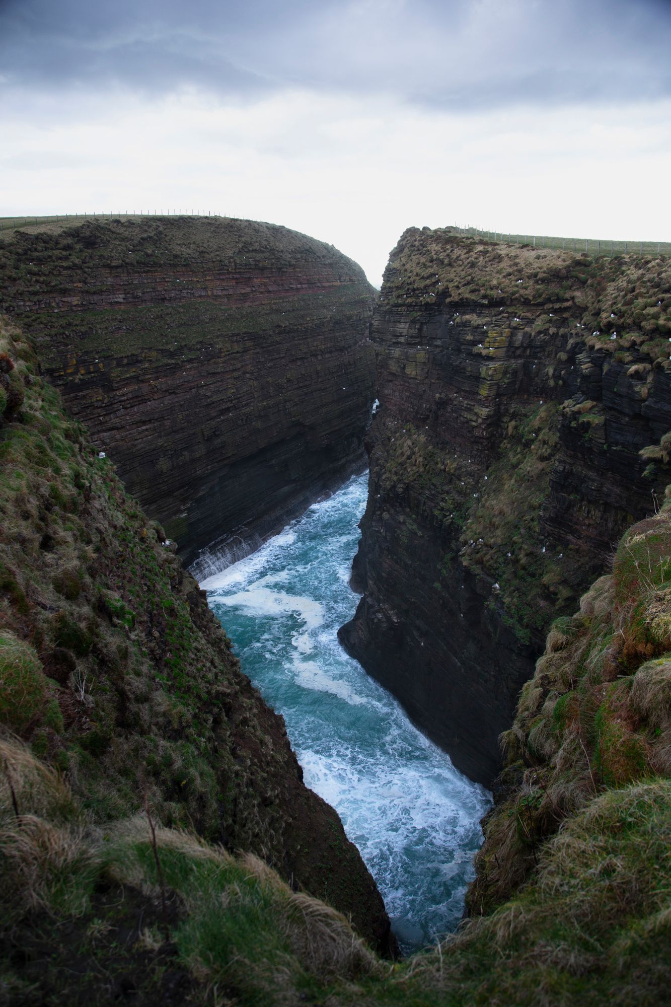 Dramatic coastal gorge with steep cliffs and rushing blue waters crashing through the narrow canyon in Scotland.