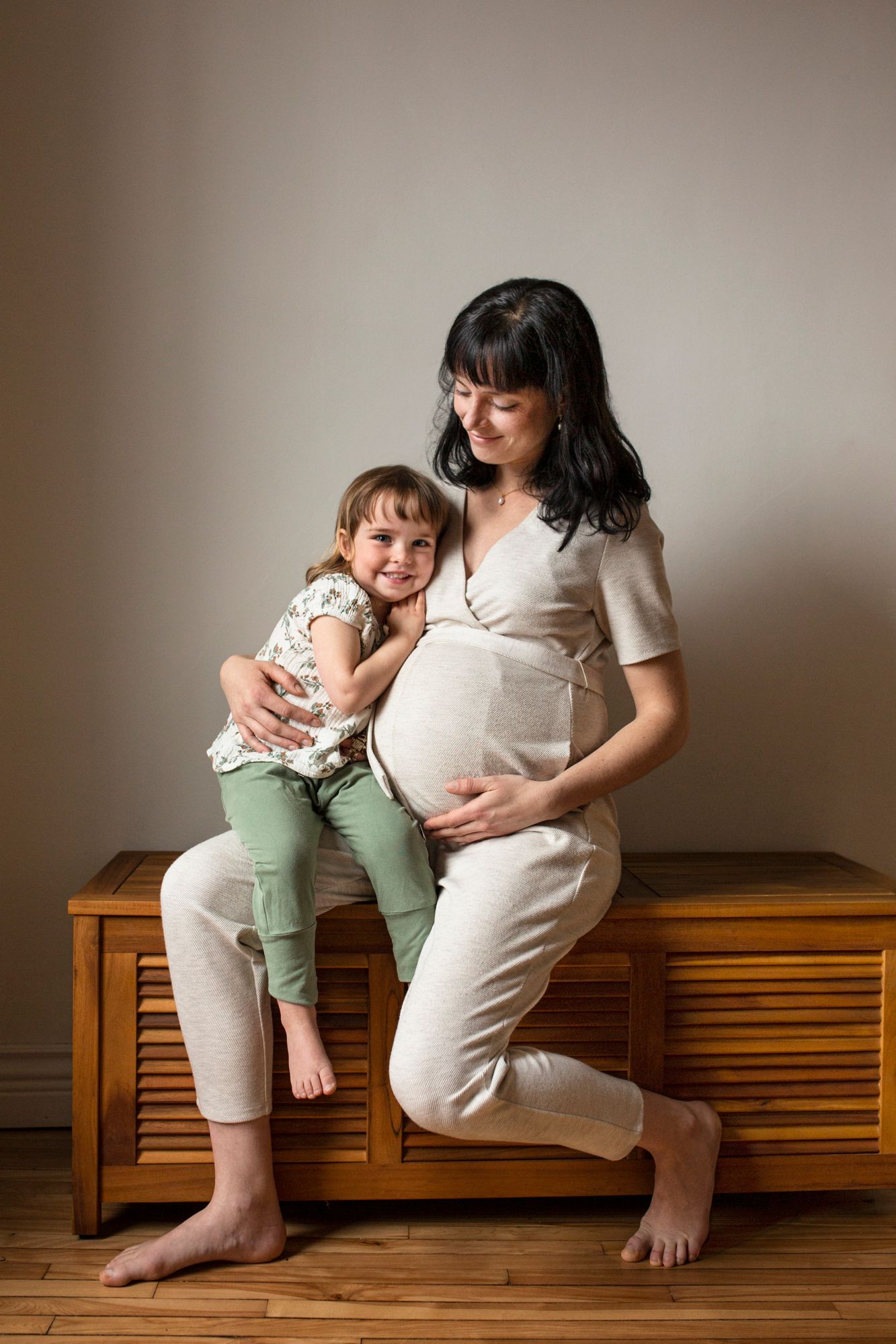 A tender maternity photoshoot series showing a parent and child sitting together on a wooden bench in matching outfits.