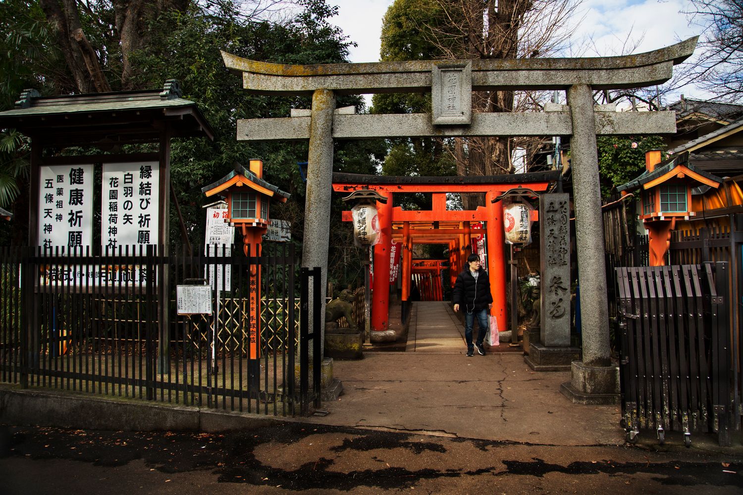 Red torii gates and temple buildings along a shaded pathway in Japan.