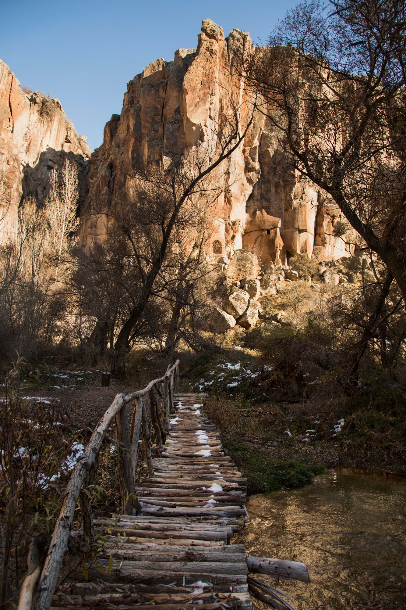 Winding wooden walkway leads through rocky cliffs and cave dwellings in Cappadocia.