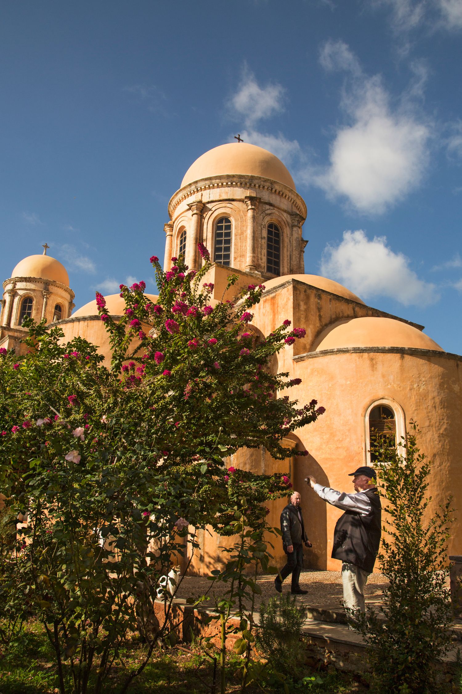 Ornate peach-colored church domes and bougainvillea flowers against a bright blue sky.