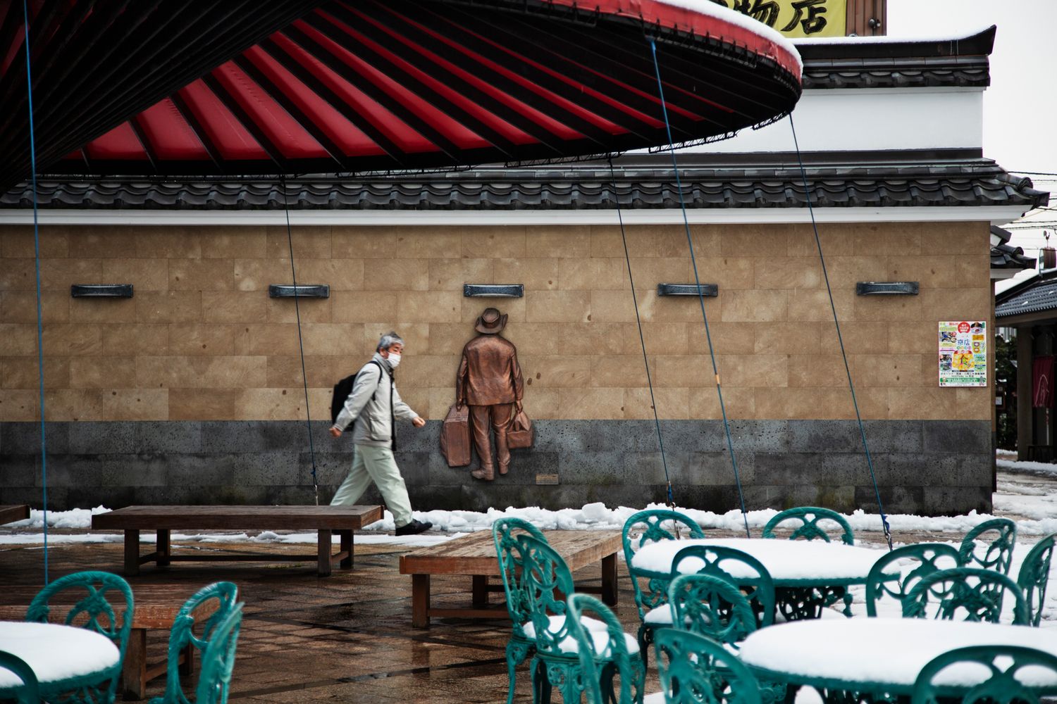 Outdoor cafe space with turquoise chairs and red umbrellas covered in snow.