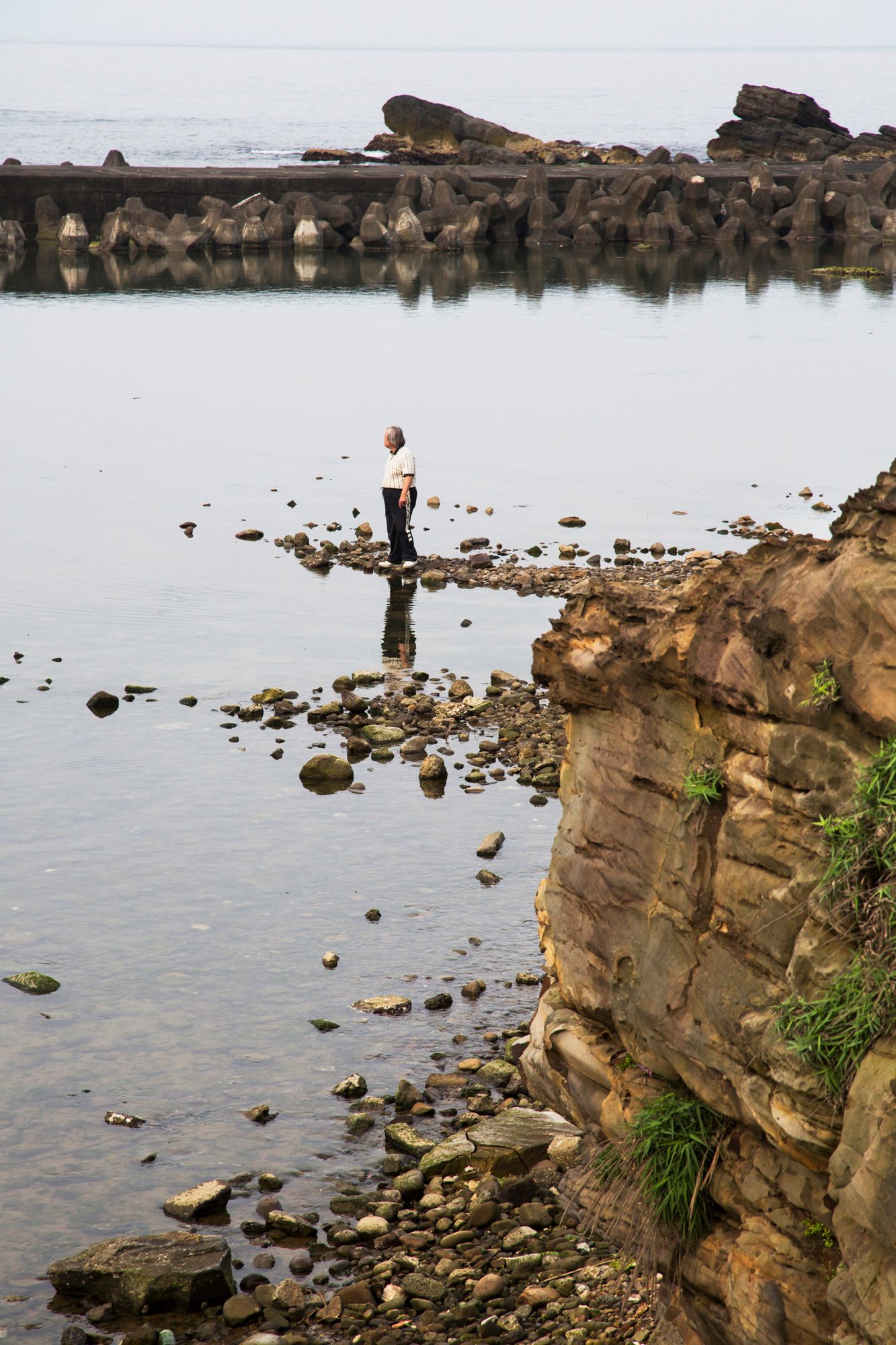 Eroded sandstone cliffs meeting calm water with scattered rocks along the shoreline.