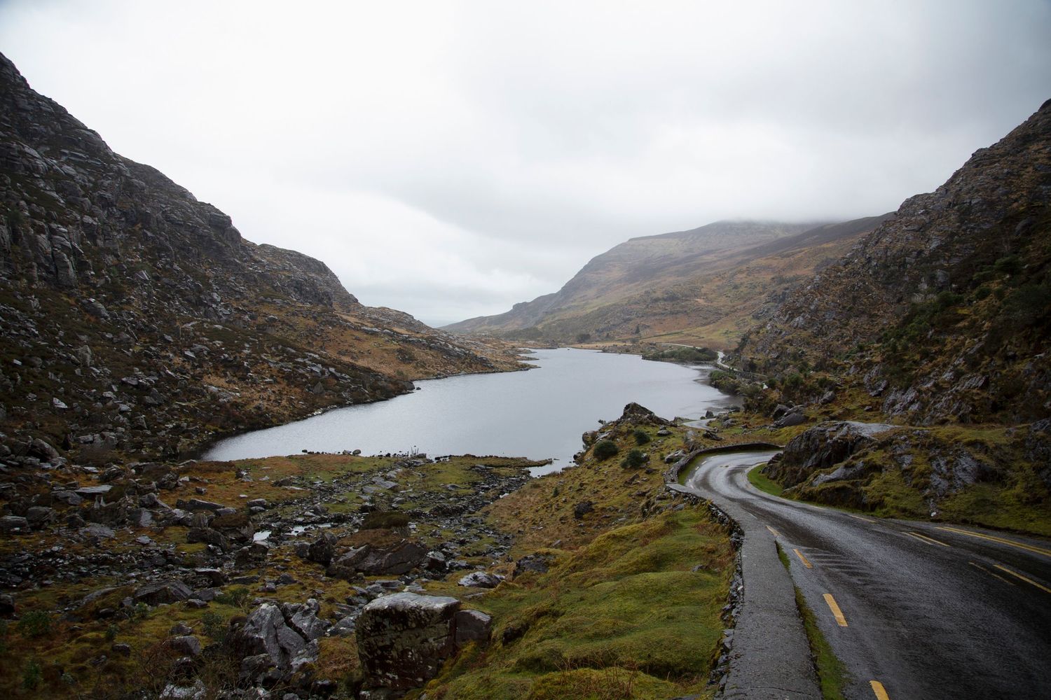 Winding mountain road cuts through rocky terrain in misty weather conditions.