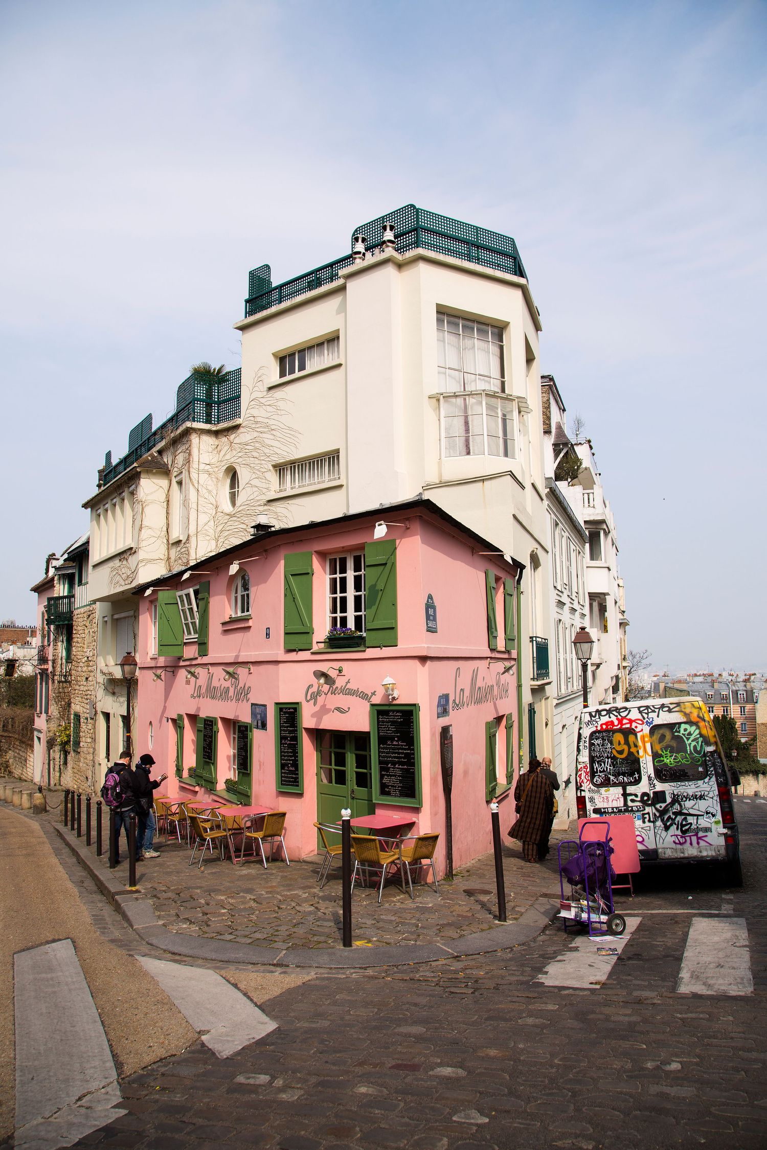 Charming pink cafe with green shutters on a cobblestone street corner in Montmartre, Paris.