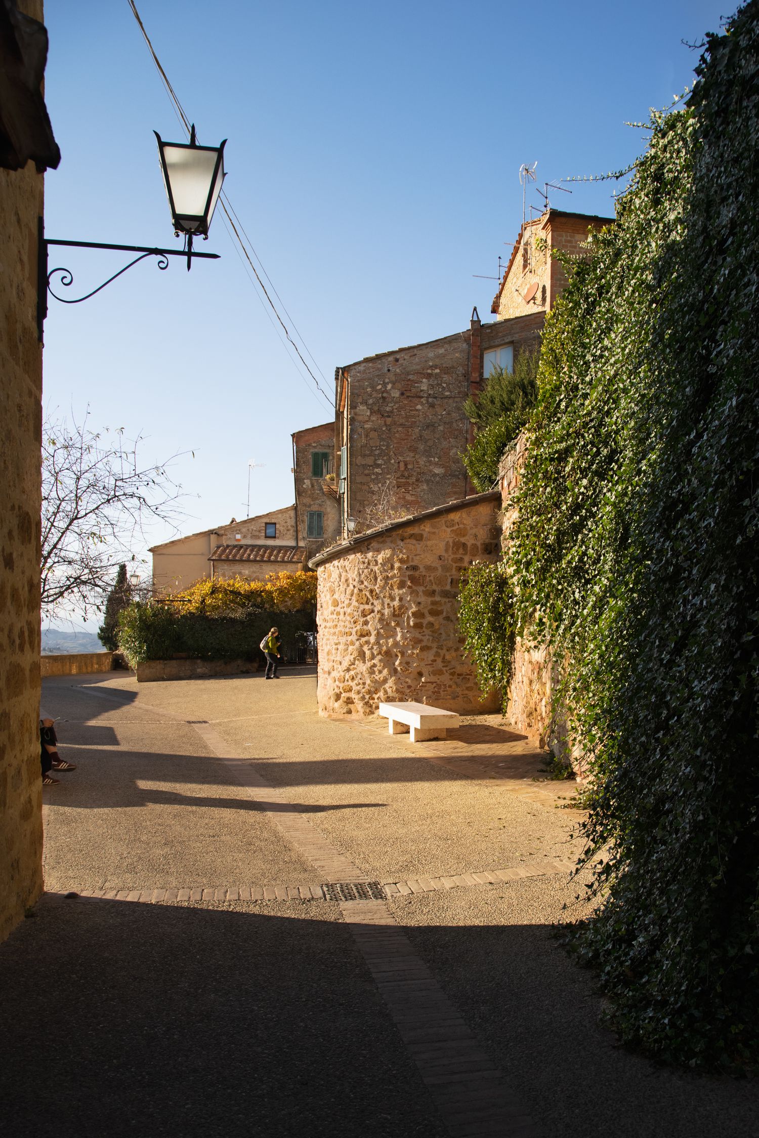 Sunlit stone alley in a medieval village with ivy-covered walls, a vintage lantern, and a cyclist in the background.