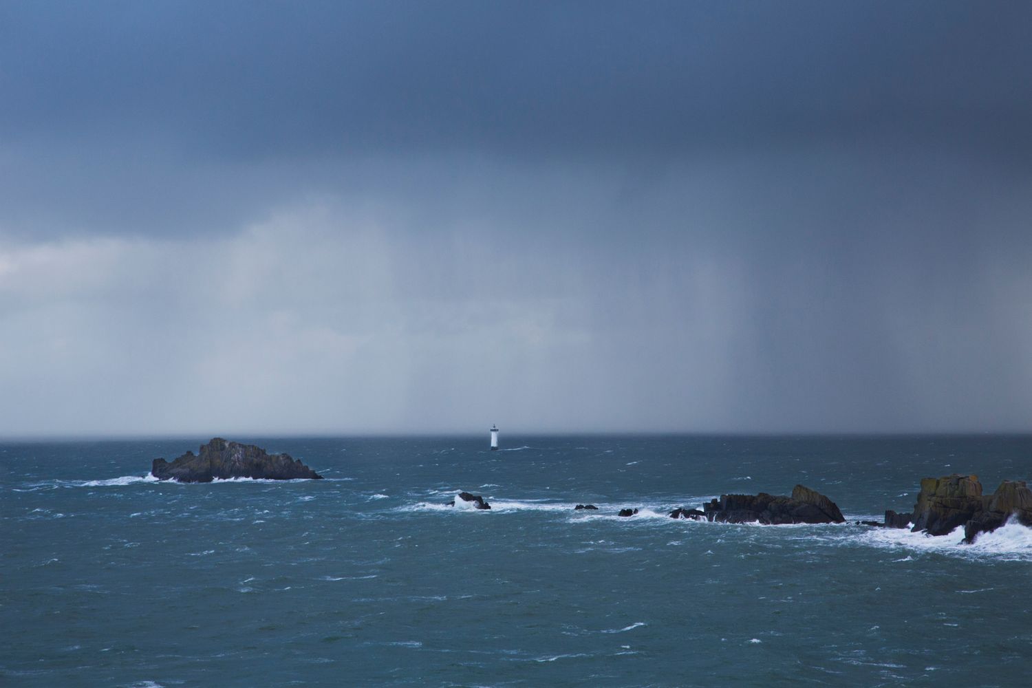 Rocky coastline with crashing waves against rugged cliffs under moody sky and ocean.
