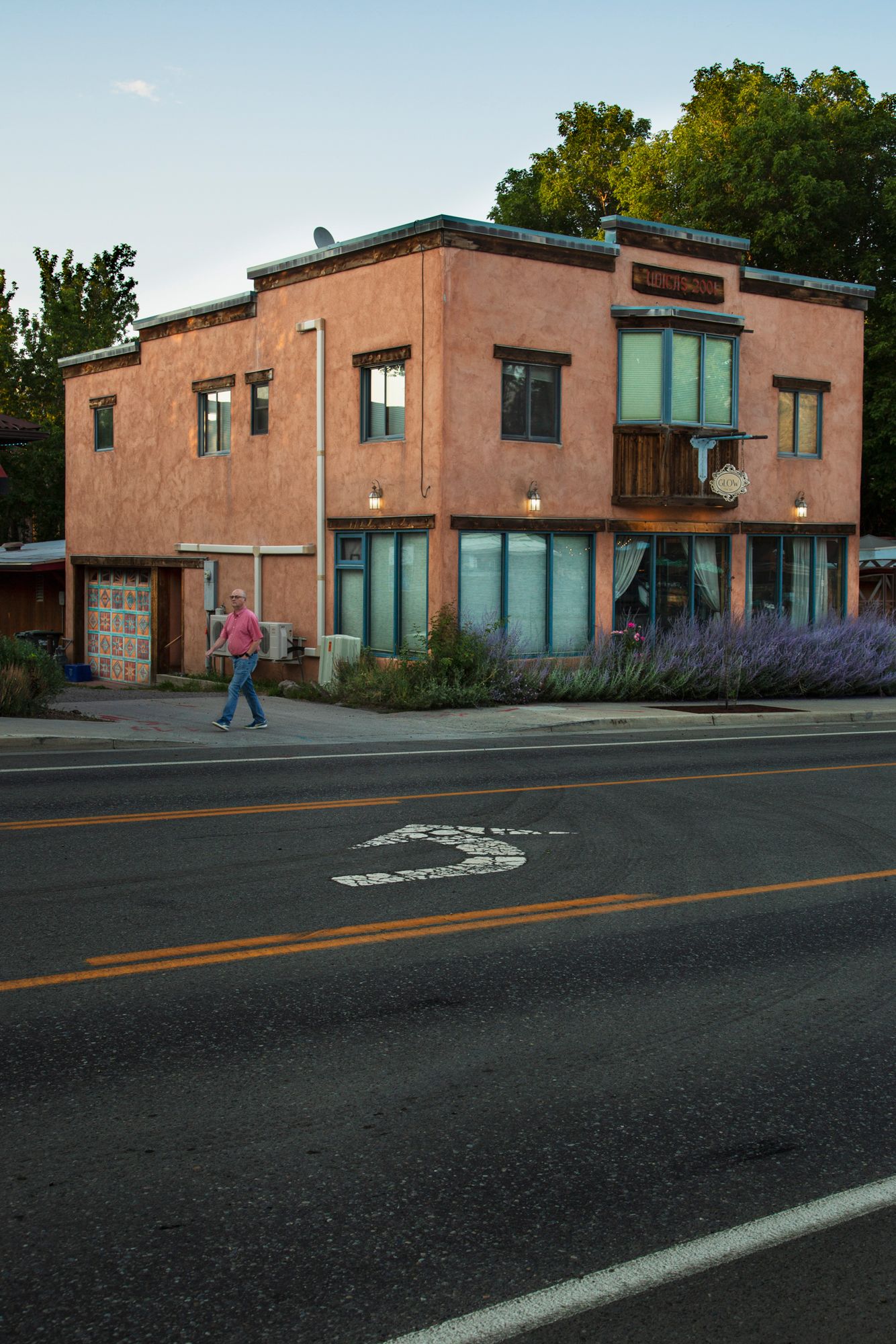 Adobe style building with turquoise windows and a person walking along a desert road at dusk.