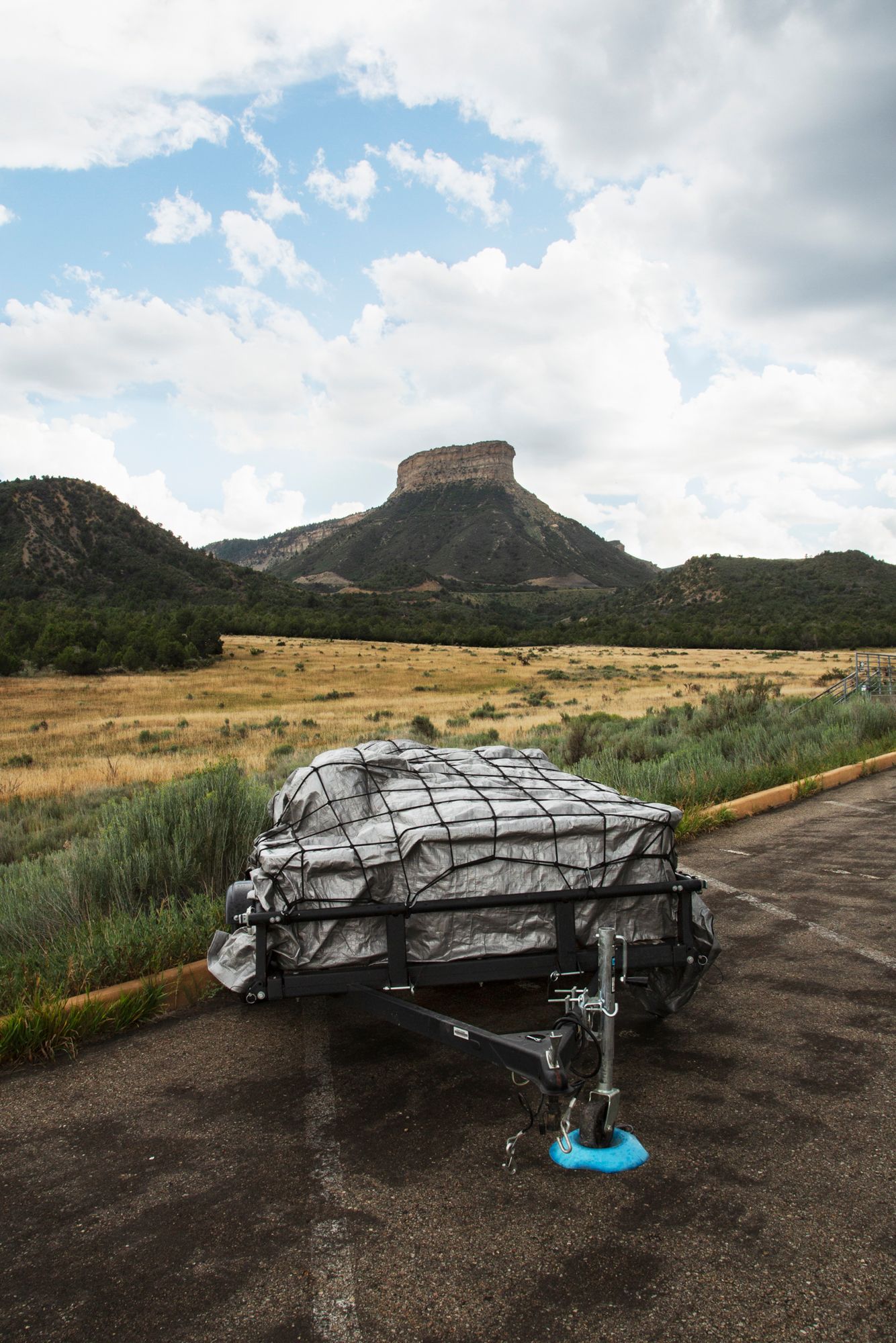 A covered boat trailer sits in a parking lot with a distinctive mesa formation visible in the desert landscape background.