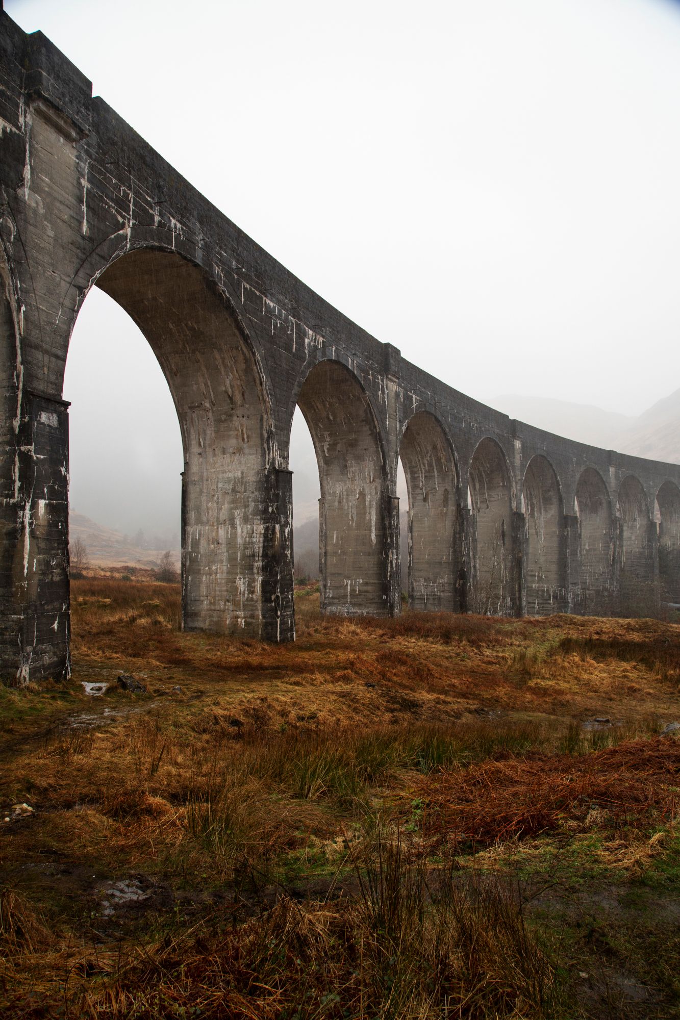 Majestic stone railway viaduct stretches across misty Scottish moorland with dramatic arches in foggy conditions.