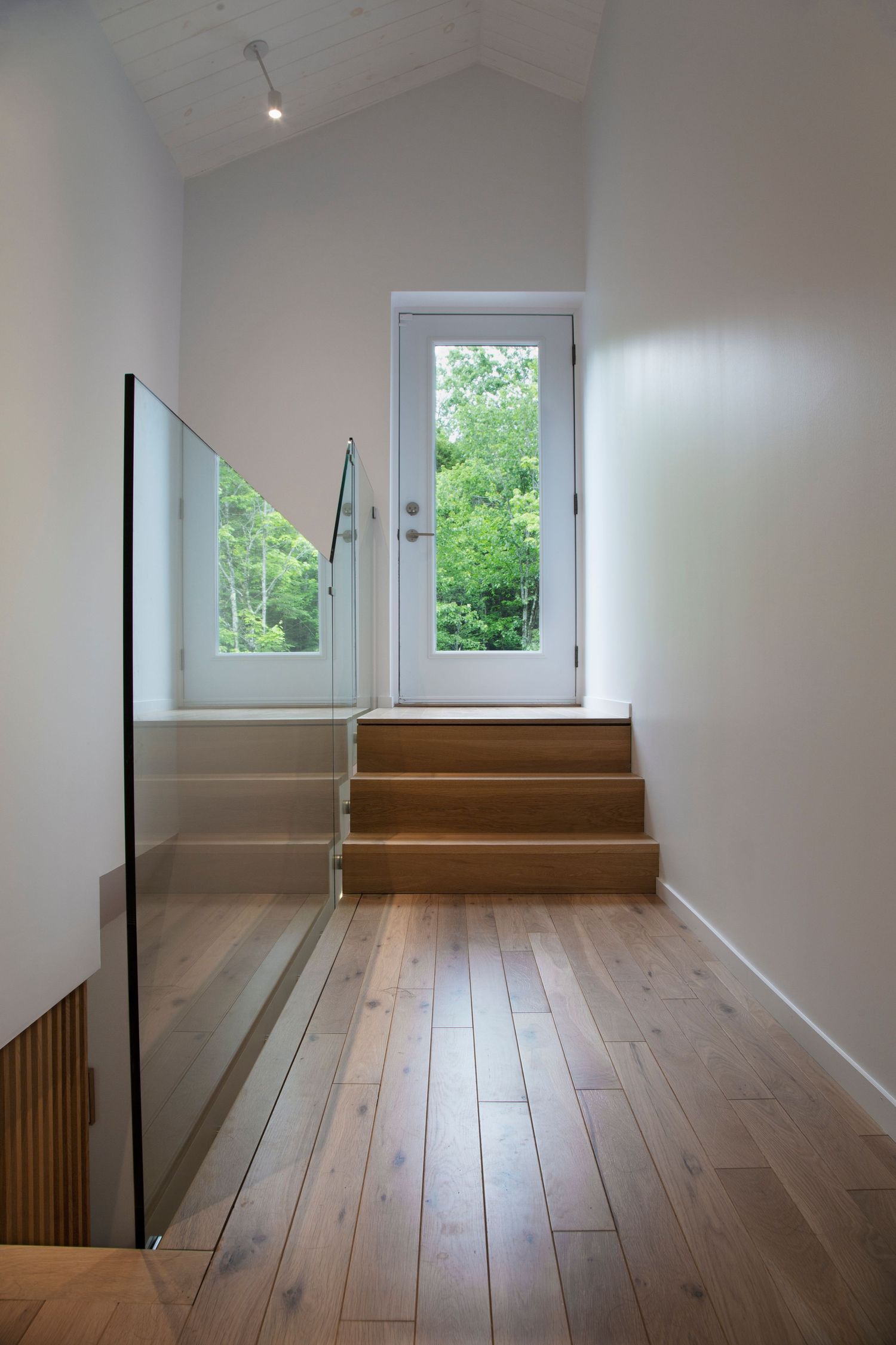 Minimalist interior space with wooden flooring and steps leading to a window with natural light.