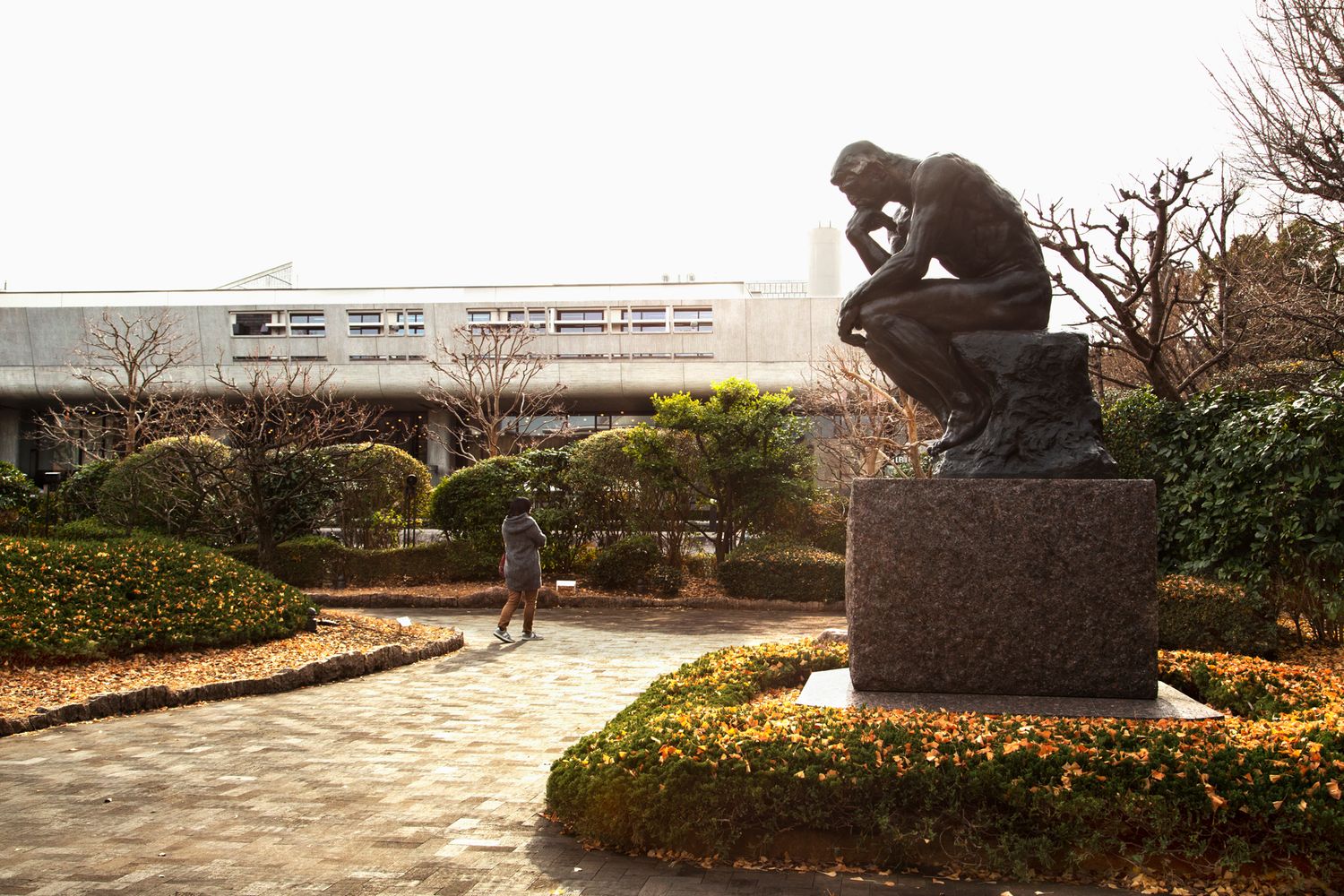 Bronze statue in a manicured garden with yellow flowers and pathways.