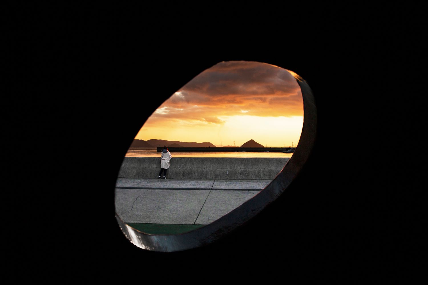 Dramatic sunset sky viewed through dark tunnel or underpass opening.