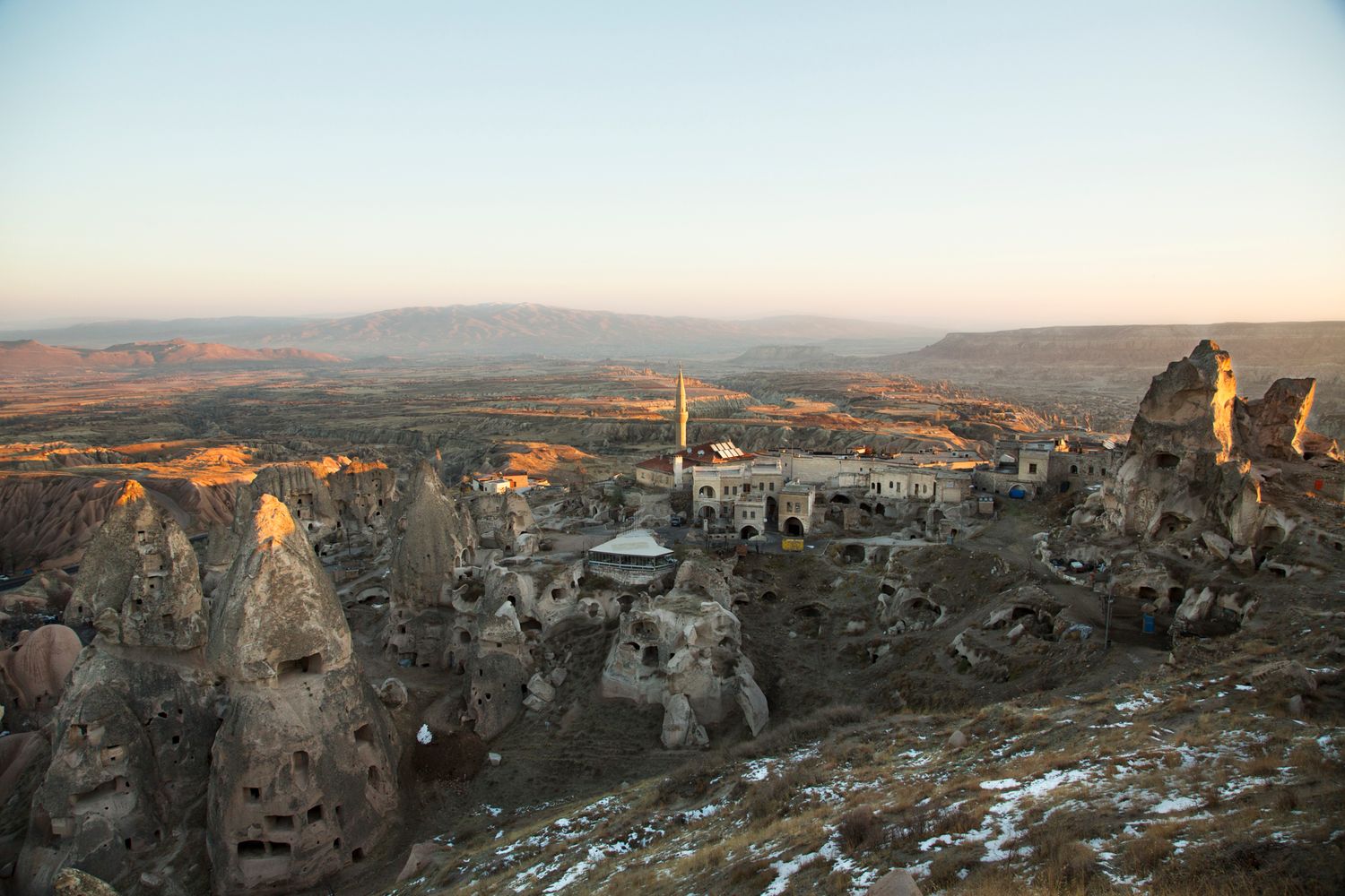 Snow-dusted landscape of ancient cave dwellings and rock formations at sunset.