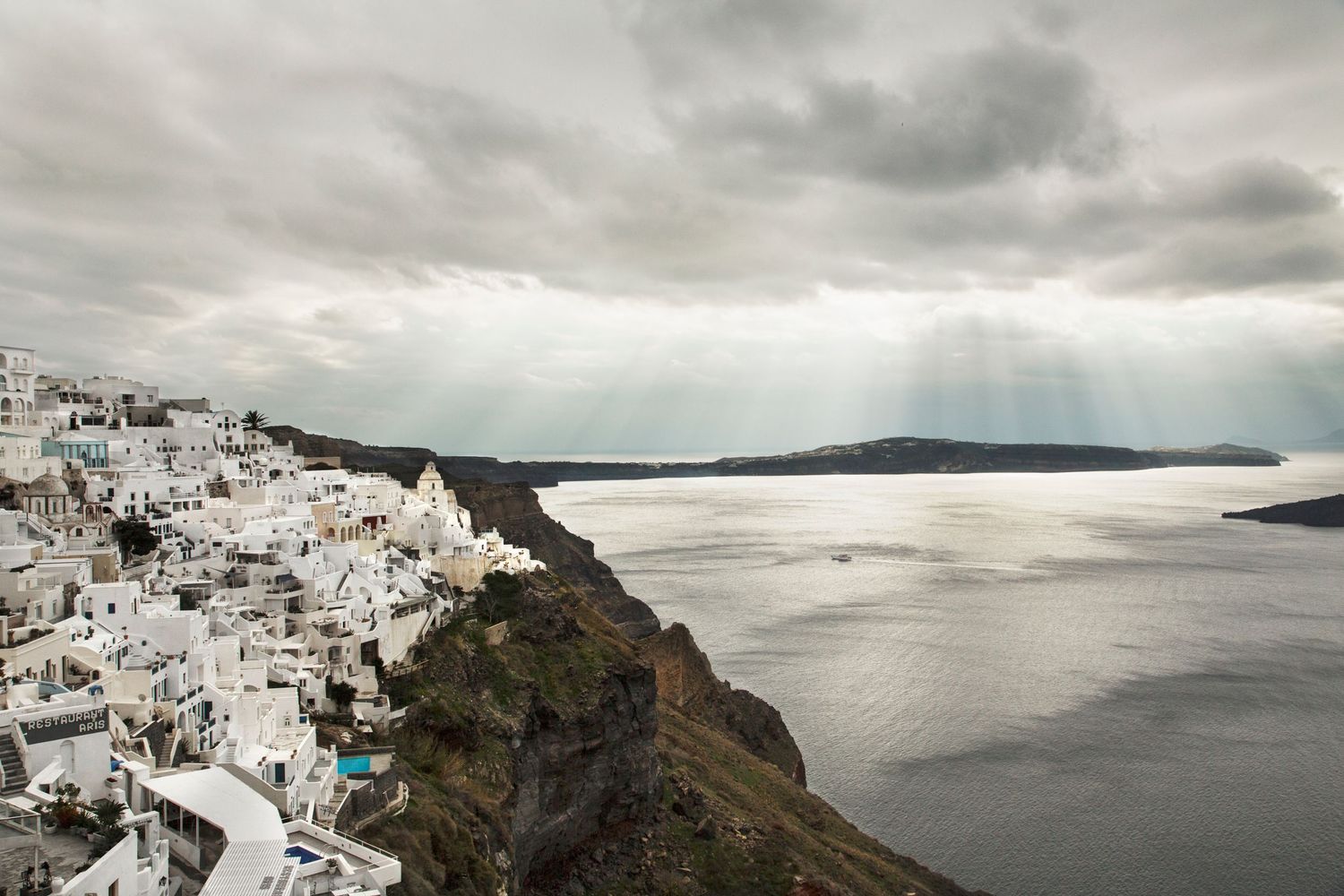 Panoramic view of Santorini's white buildings cascading down volcanic cliffs at sunset.