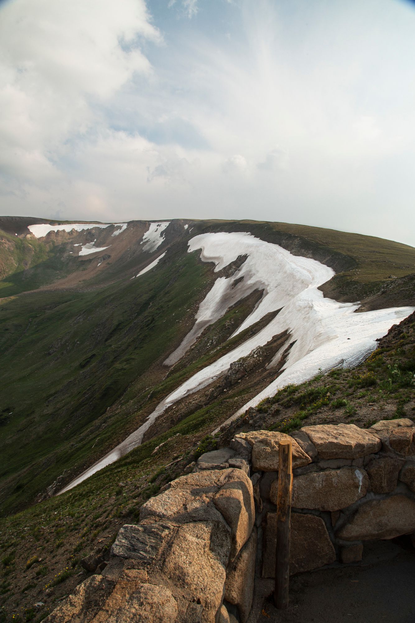 Snow patches cling to steep mountain slopes beneath cloudy skies along a rugged rocky ridgeline.