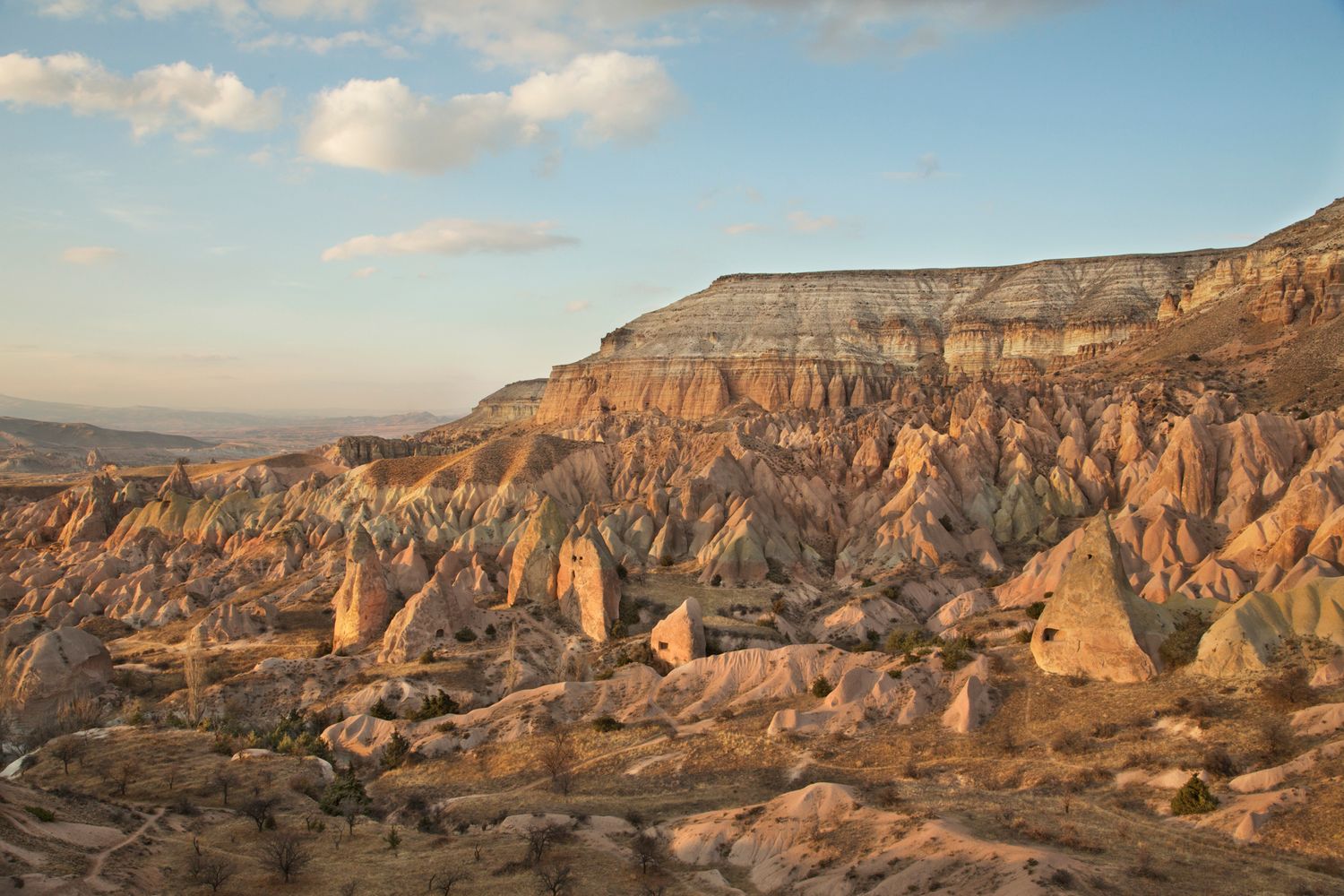 Dramatic rock formations and cliffs in Cappadocia, Turkey illuminated by warm sunset light against a blue sky.