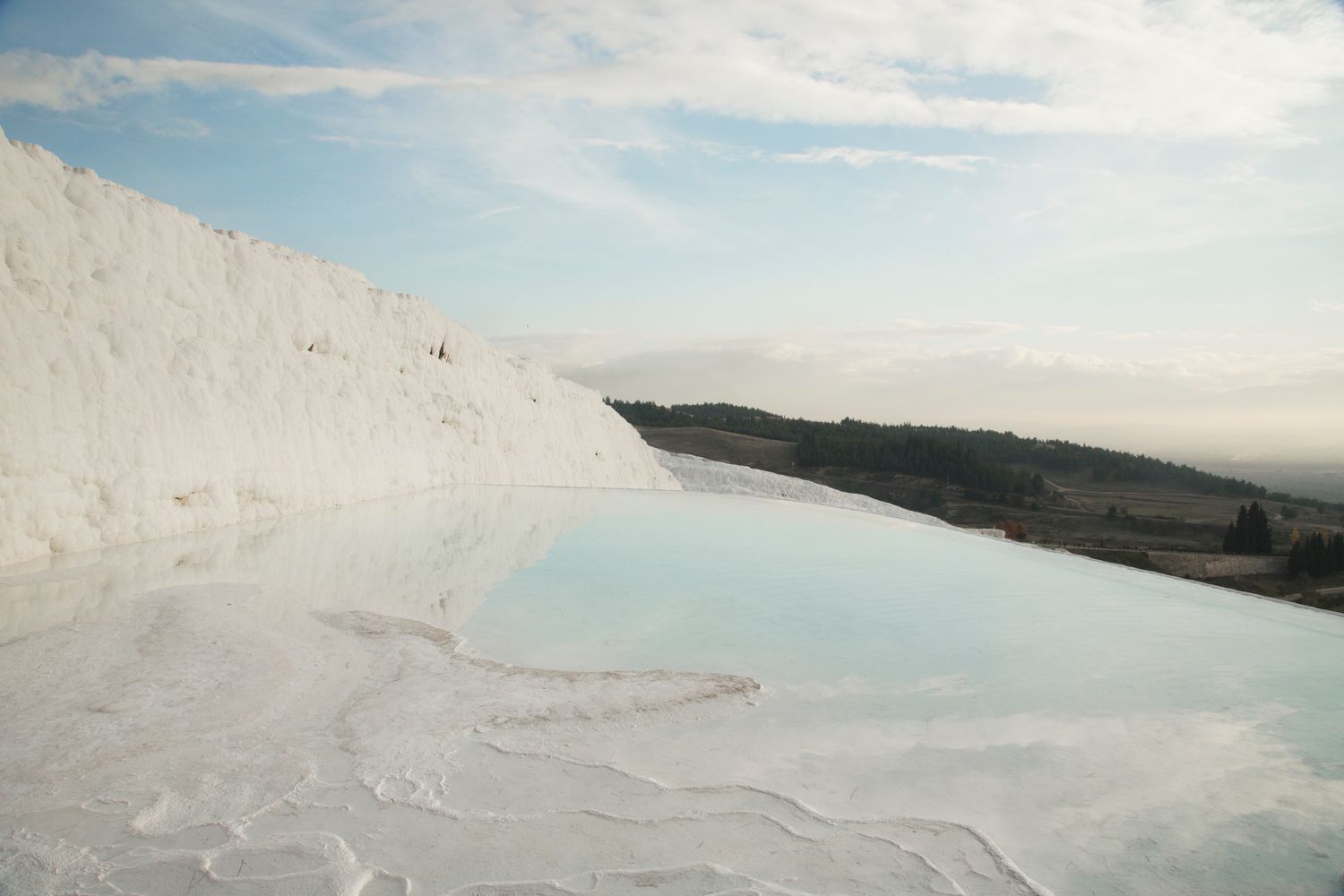 Turquoise thermal pools with white calcium deposits at Pamukkale terraces in Turkey under blue sky.