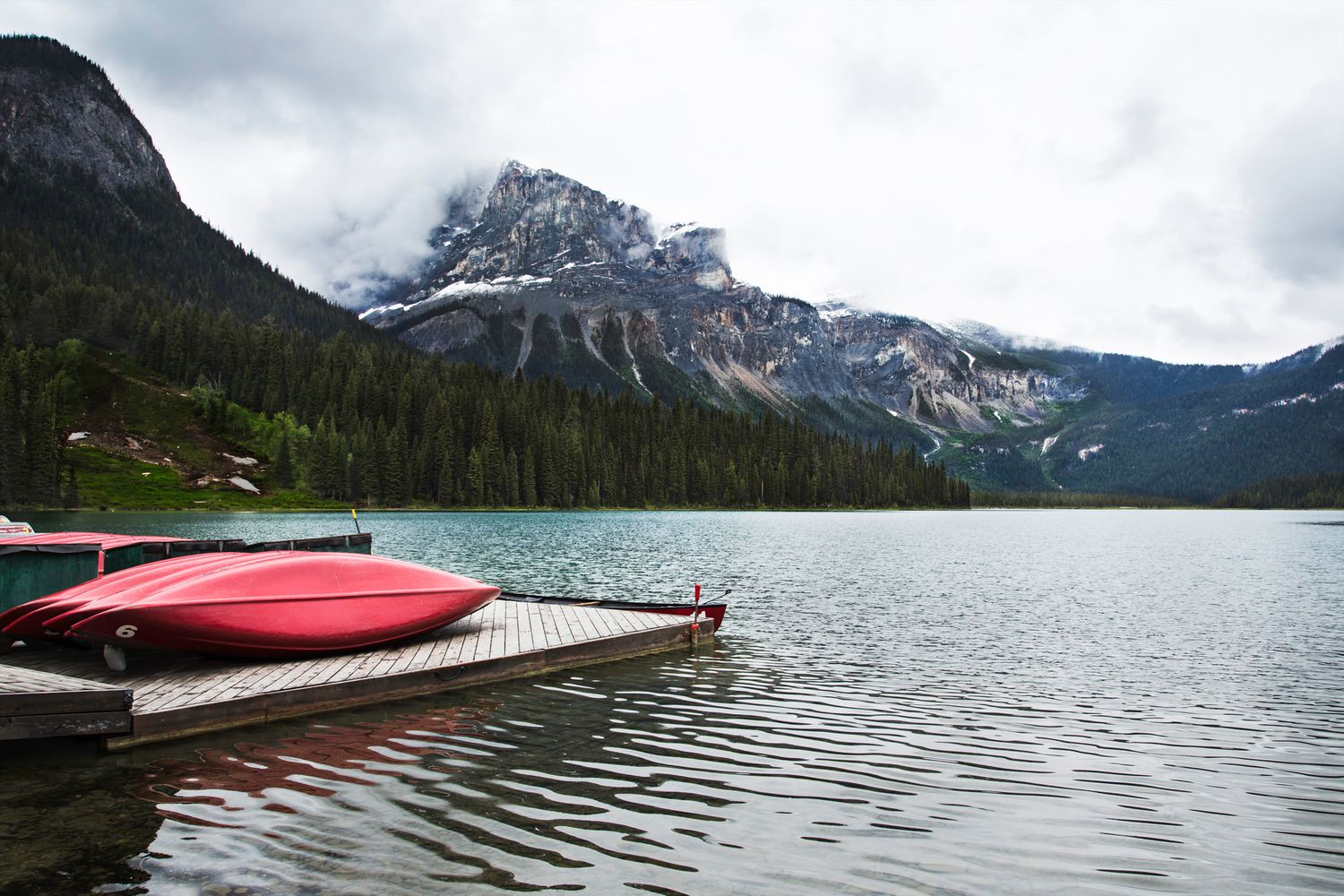 Tranquil mountain lake with dramatic cloudy skies and red canoes lined up along wooden dock.