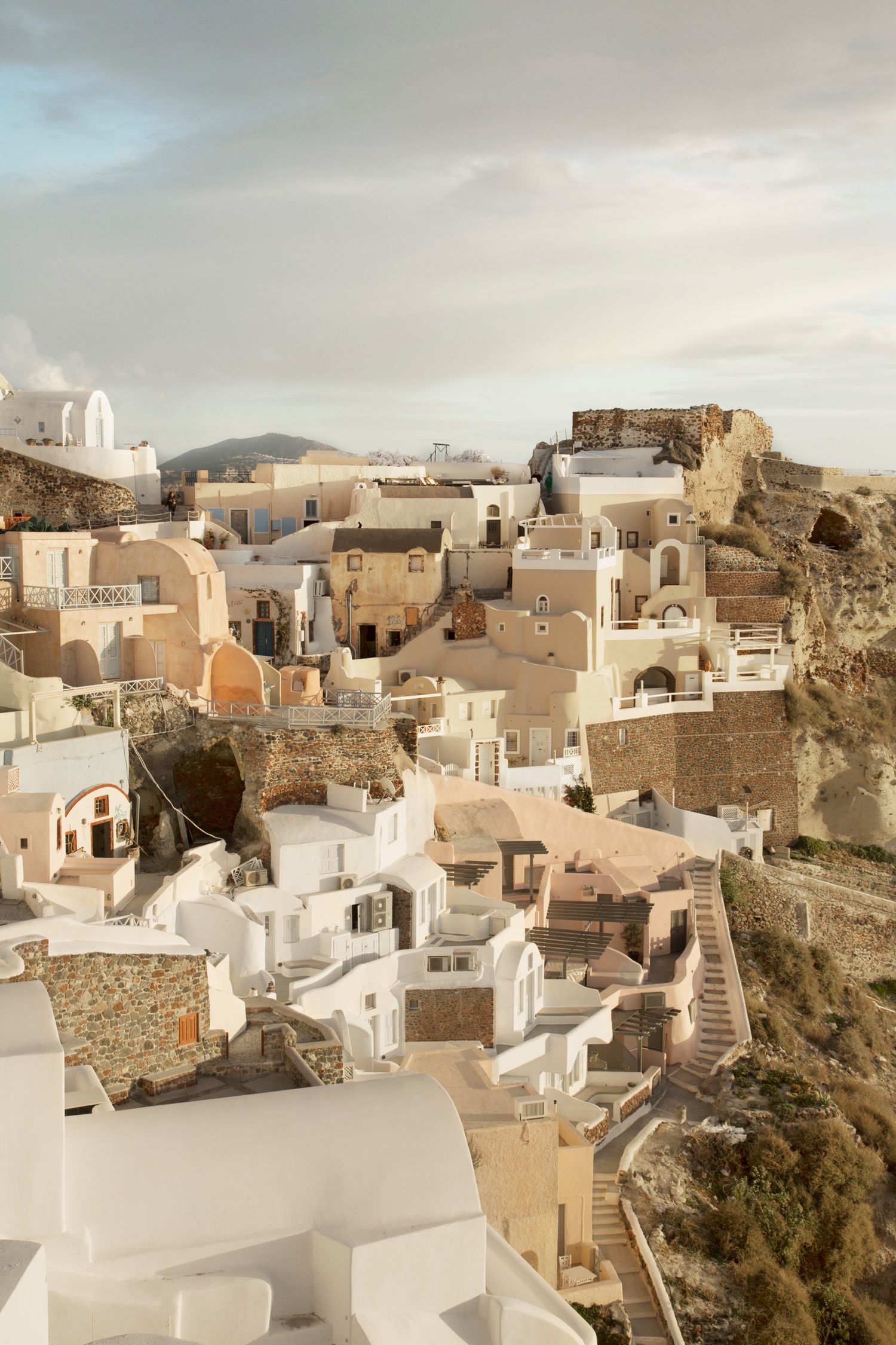 Aerial view of white-washed buildings cascading down a hillside in Santorini's traditional village architecture.
