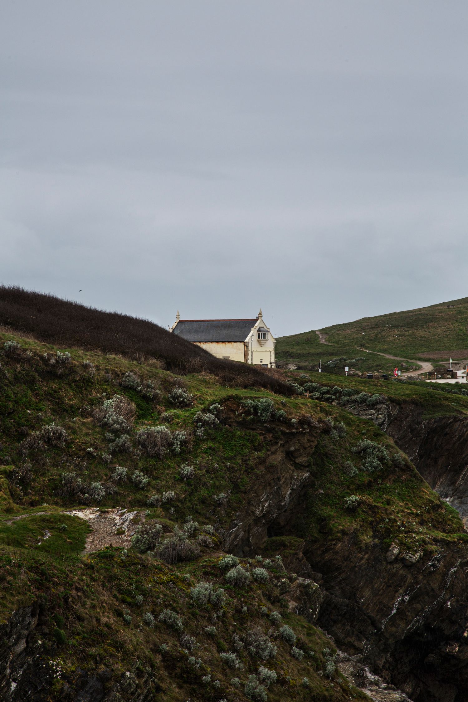 Solitary white house perched dramatically on rugged coastal cliffs under moody sky.