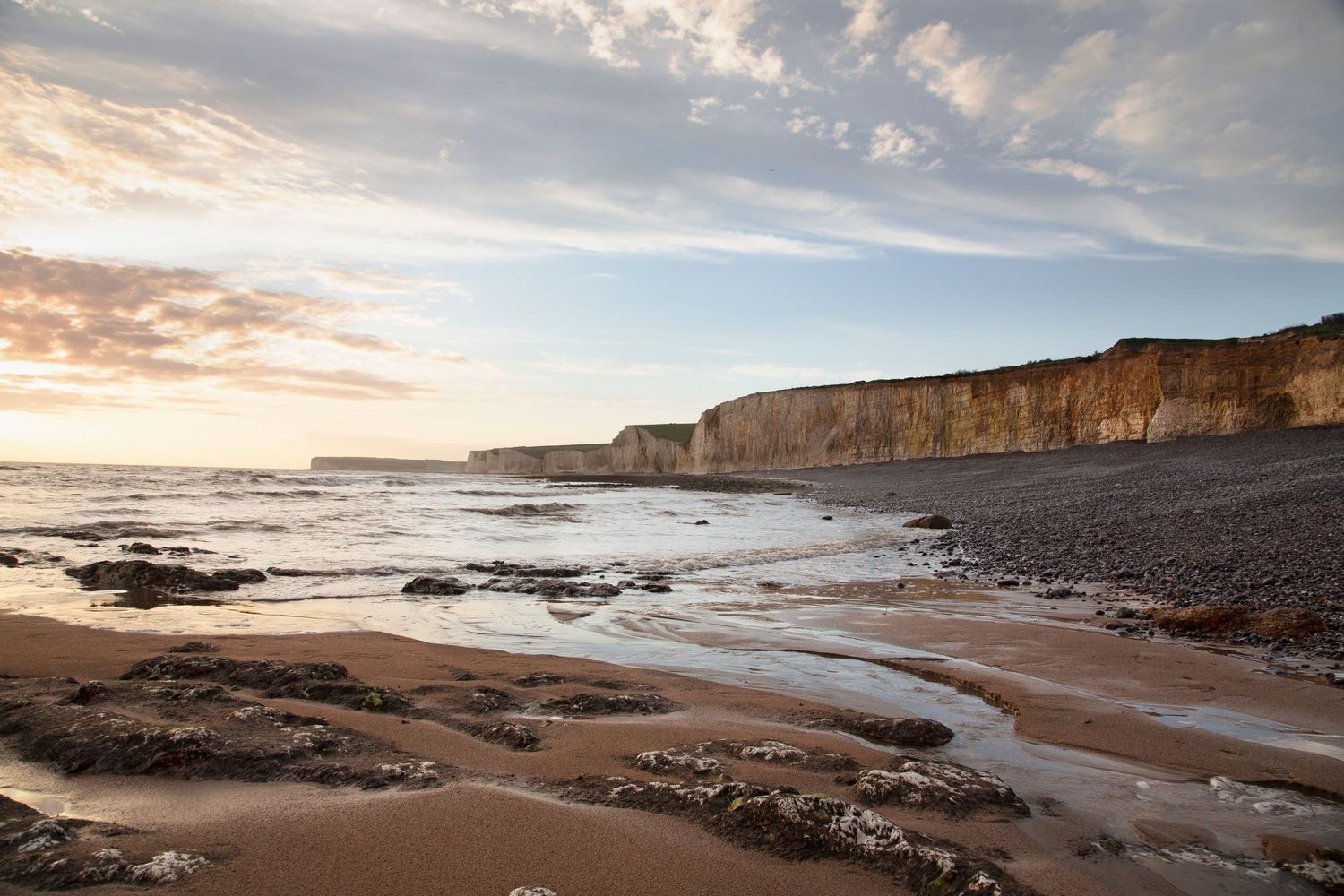 Dramatic sunset at a rocky beach with tall white cliffs and waves crashing against the shore.