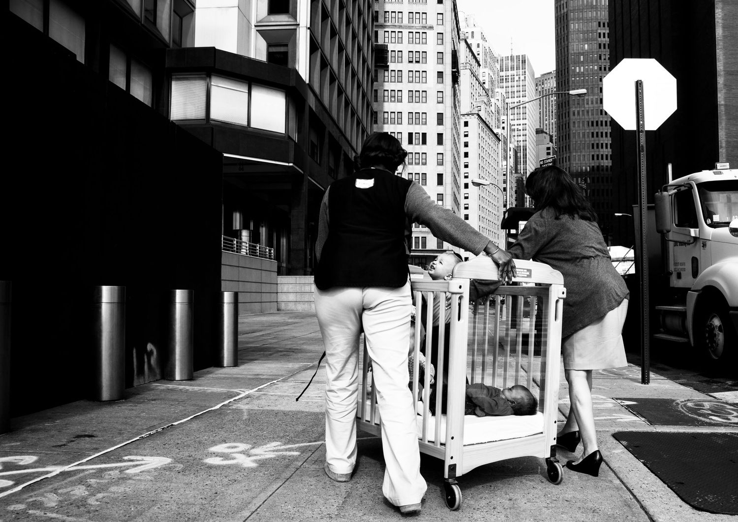 Black and white street photo of people pushing a cart in an urban setting.