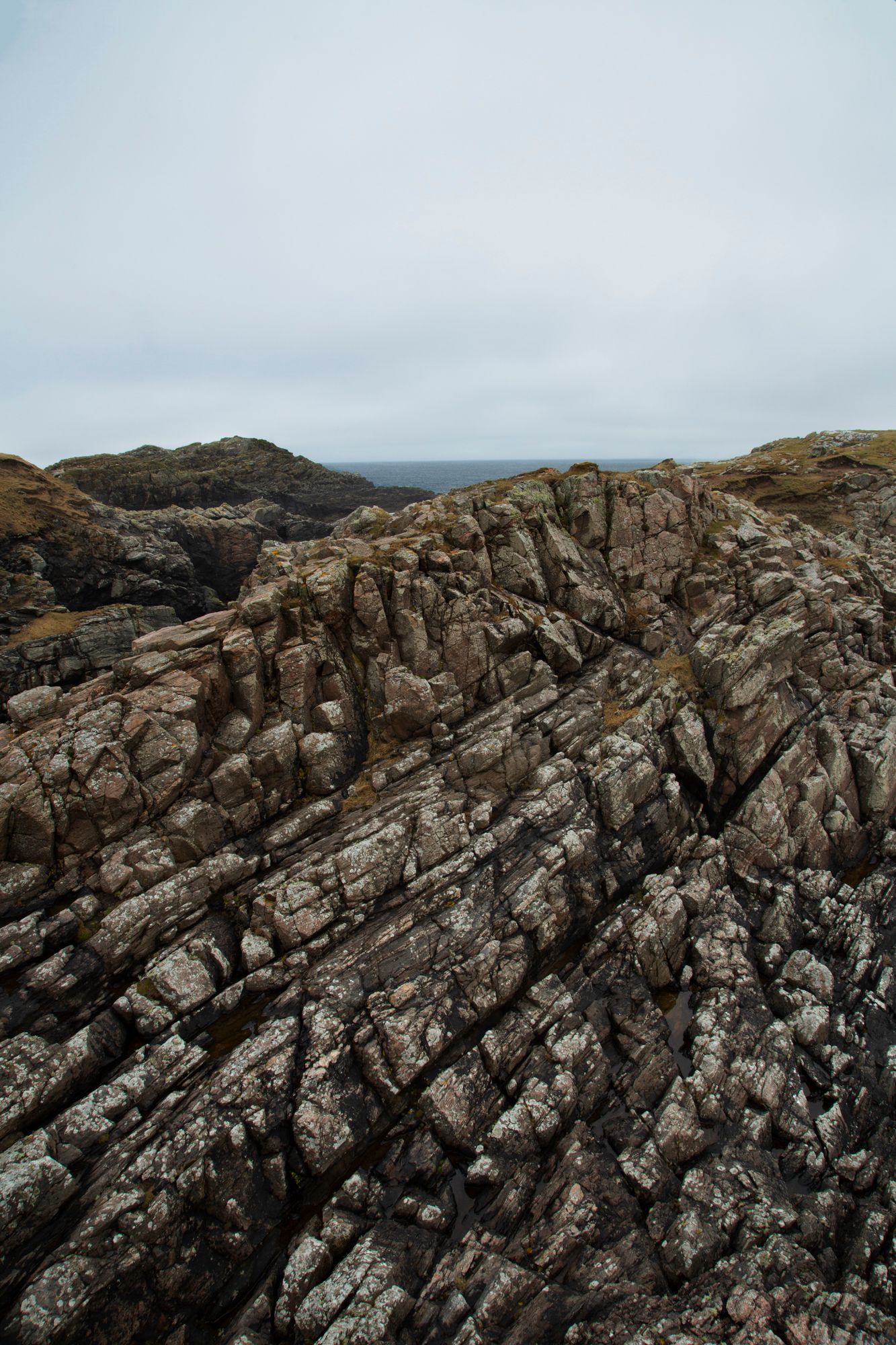 Dramatic coastal landscape with rugged rock formations and layered cliffs against a moody overcast sky.