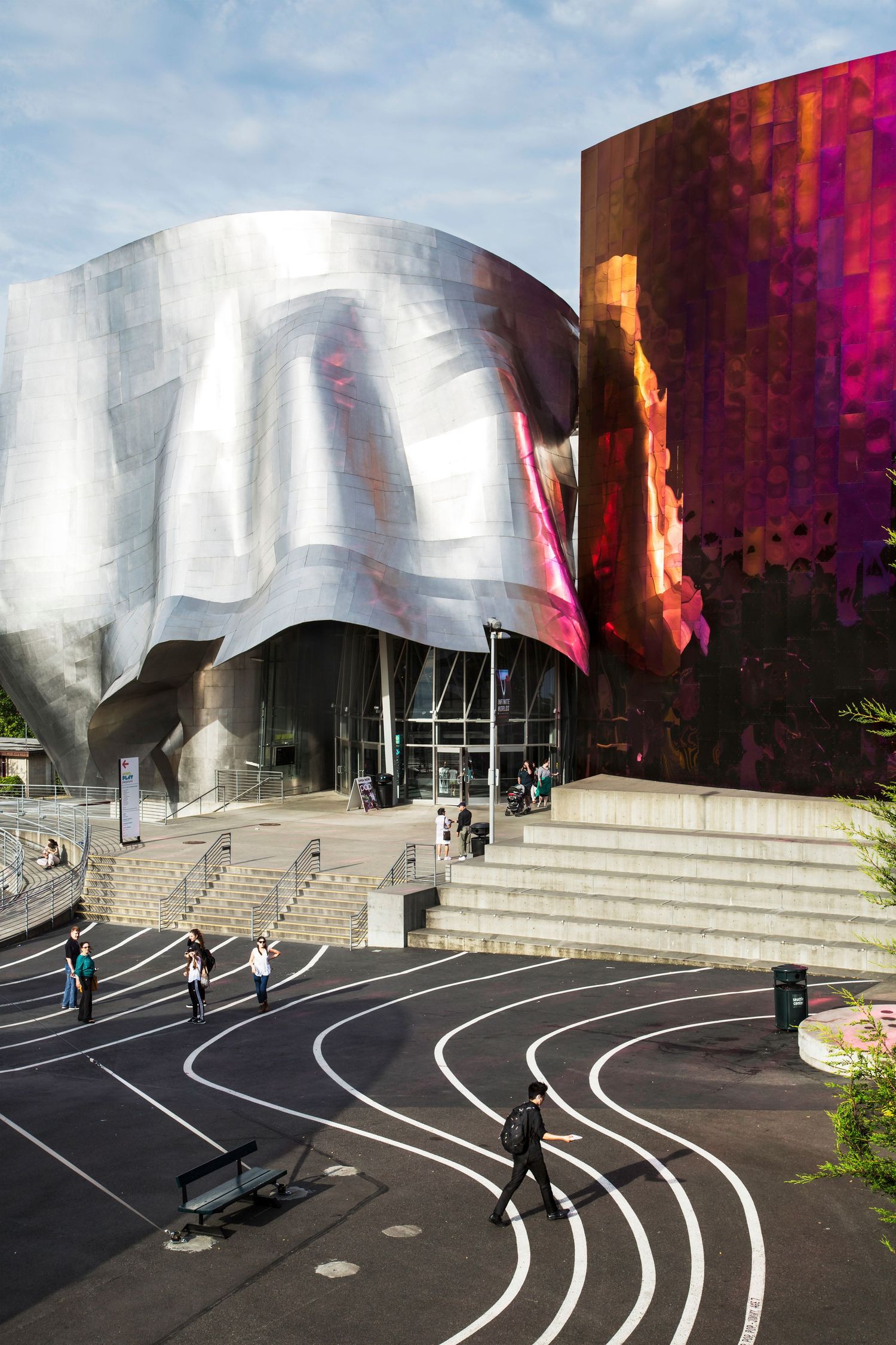 Modern silver metallic building facade with curved lines and black running track.