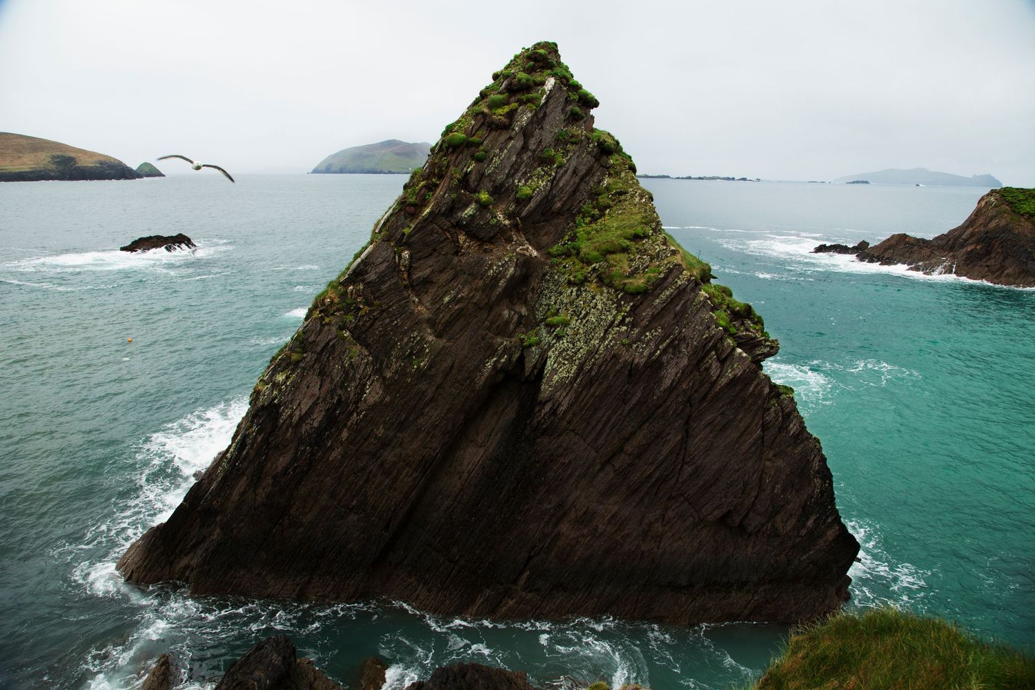 Dramatic coastal cliffs rising from turquoise ocean waters under cloudy skies.