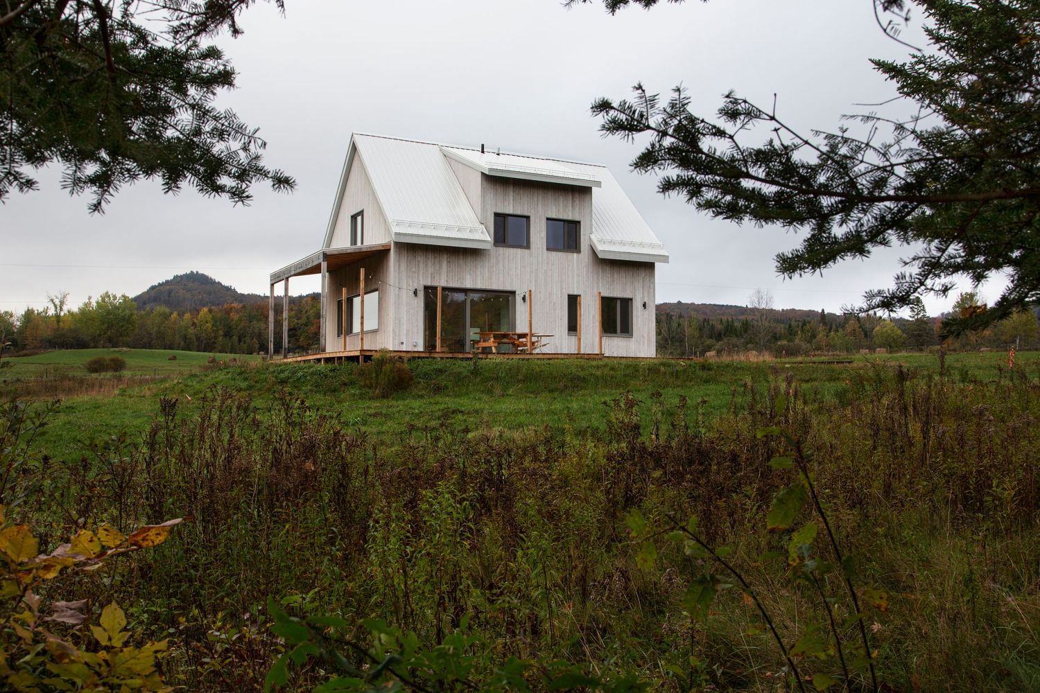 White modern farmhouse nestled on a green hillside with distant landscape views.